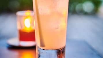 A tall glass with a straw and ice cubes, placed on a wooden surface with a candle in the background.