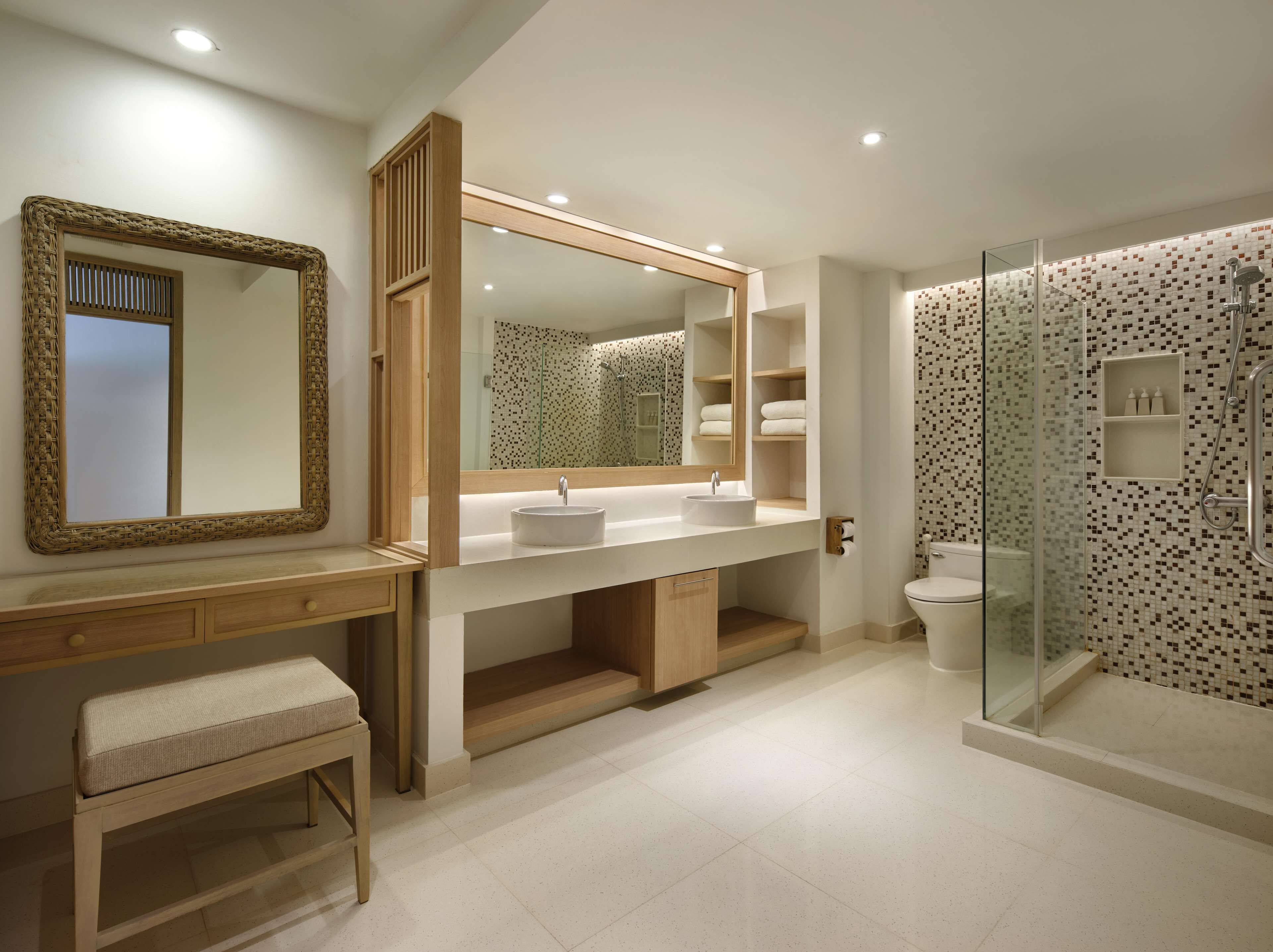 A modern bathroom with a large mirror, a sink, a bench, and a shower area.