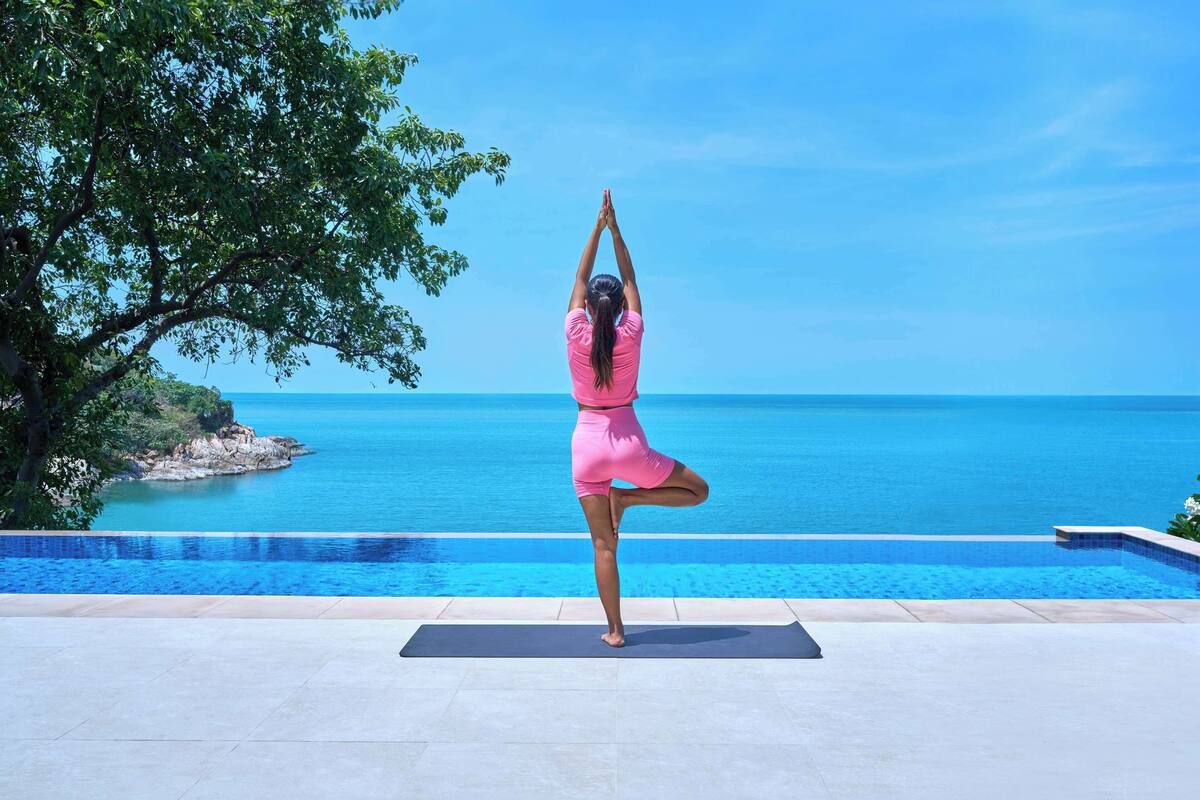 A person performing a yoga pose on a mat by a pool with a view of the ocean.