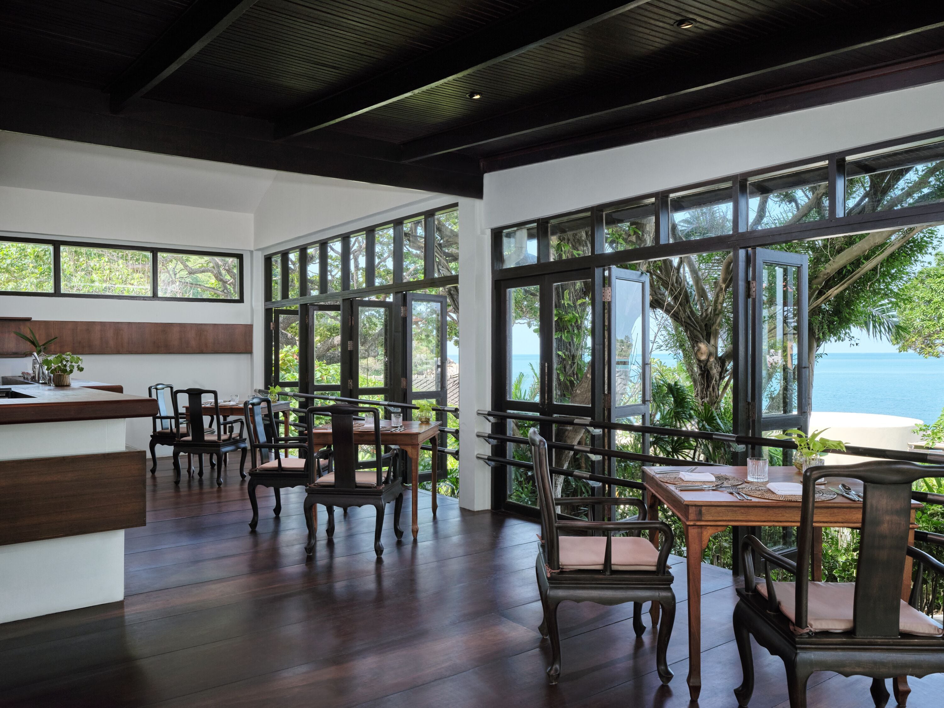 A restaurant with wooden flooring, large windows, and a view of the sea.