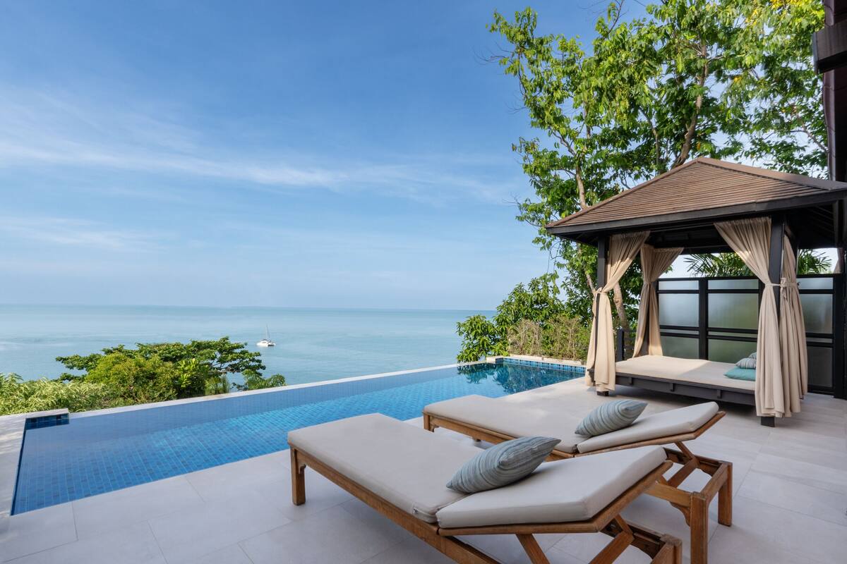 A poolside area with two lounge chairs and a canopy, overlooking a clear blue sea.