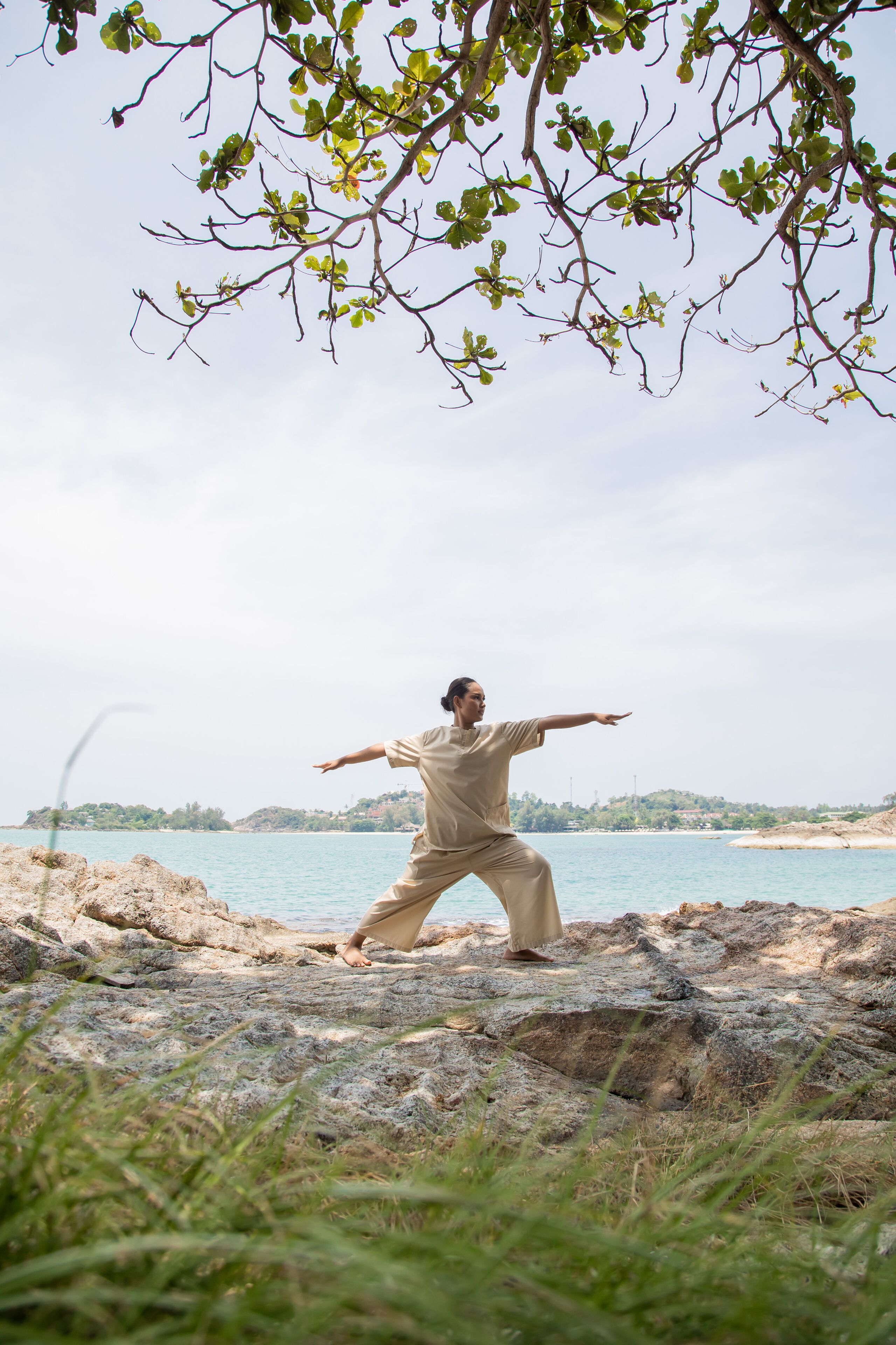 A person practicing martial arts on a rocky beach with a view of the sea and distant hills.