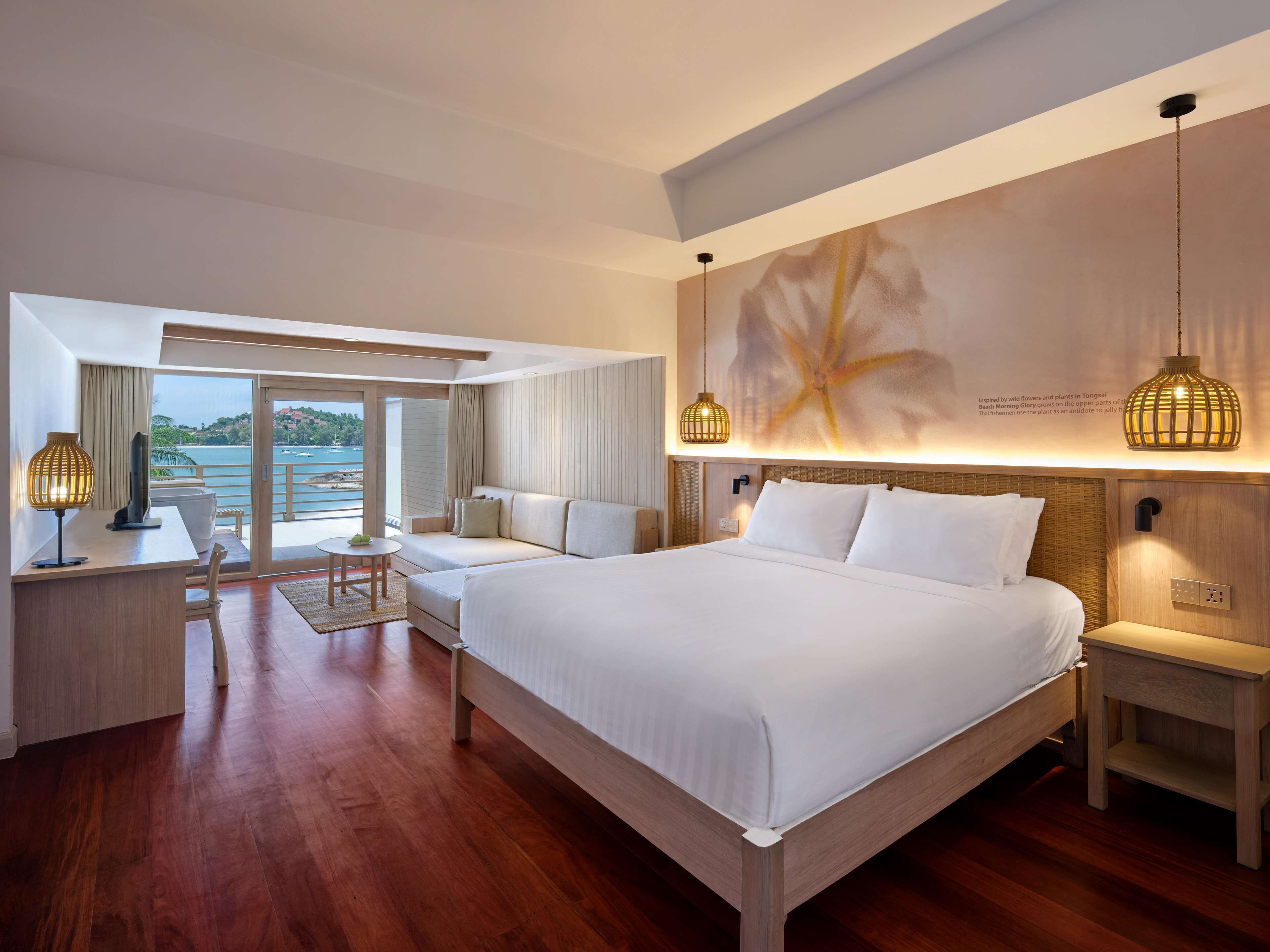 A hotel room with a large bed, a desk with a lamp, a seating area with a view of the sea, and a wall with a starfish artwork.
