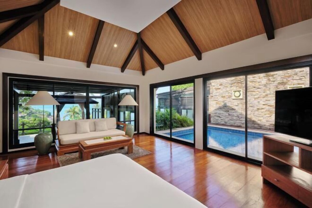 A modern interior with a large bed, a sofa, a TV, and a pool view.