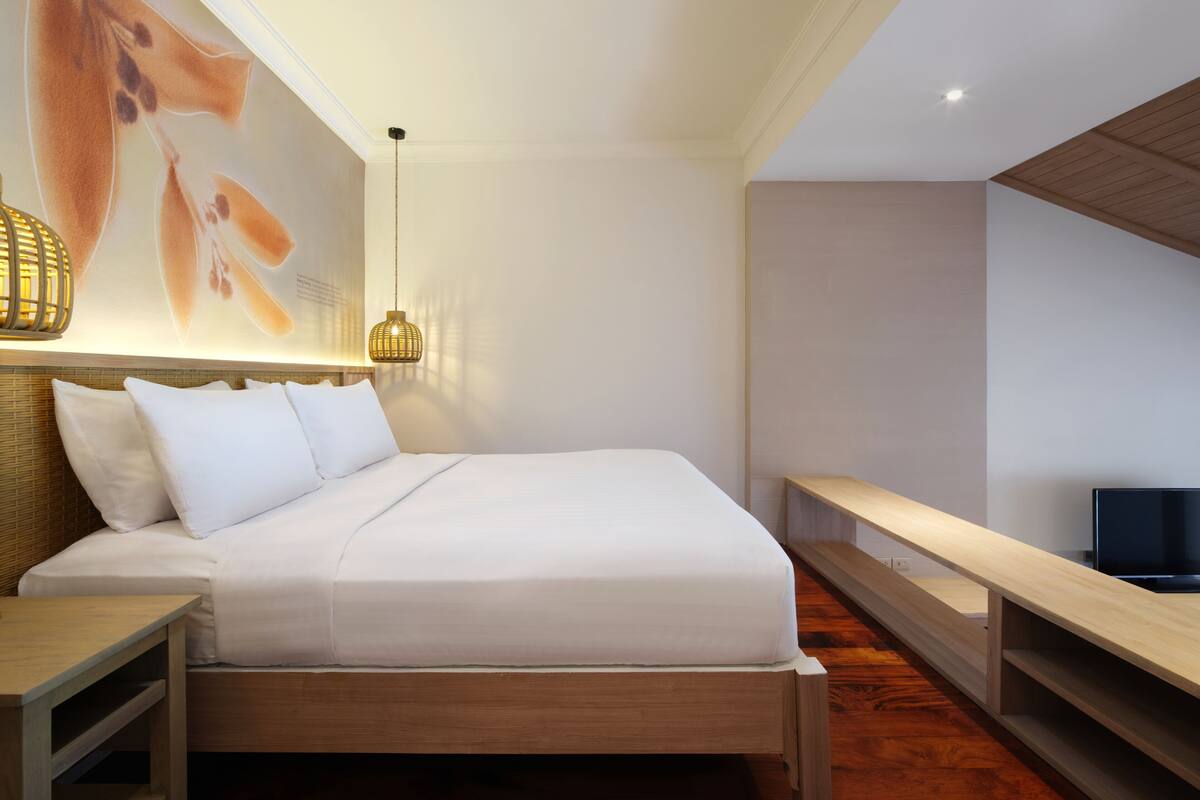 A modern bedroom with a wooden bed, a flat-screen TV, a wall-mounted light fixture, and a large abstract painting.