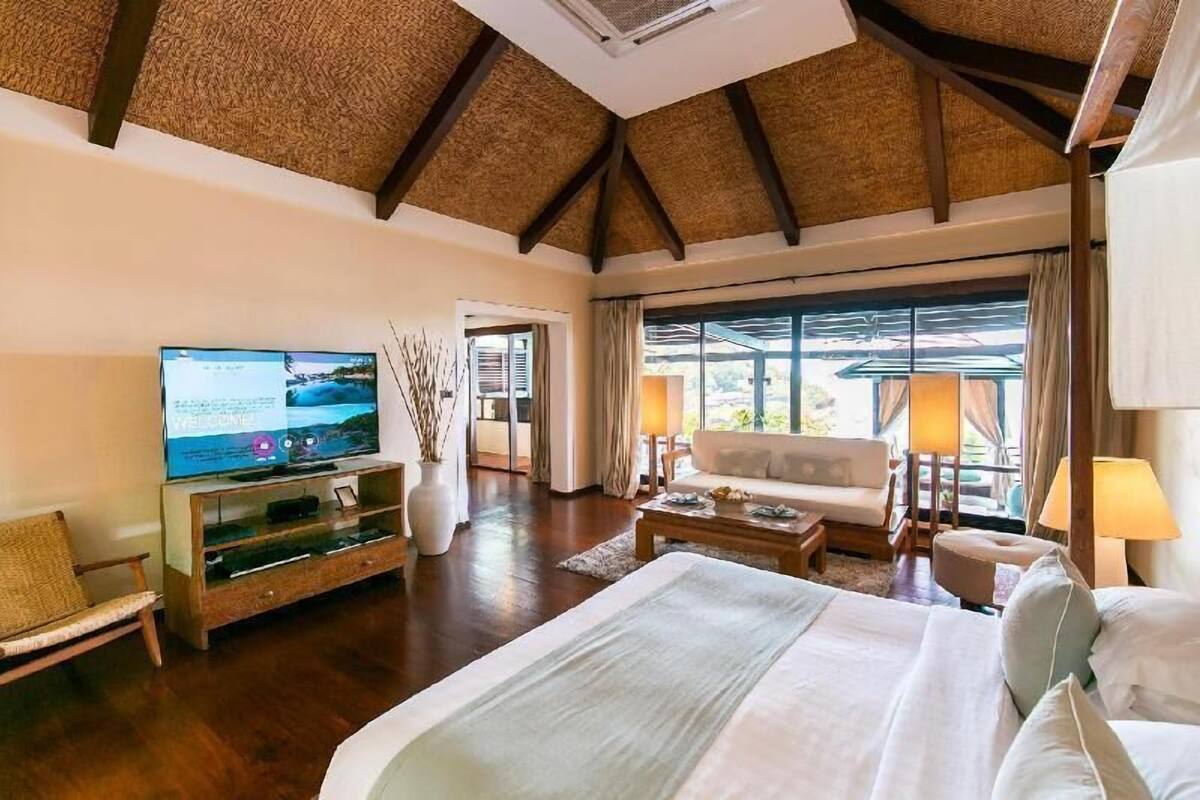 A spacious bedroom with a large bed, a television, a sofa, and a view of the outdoors.