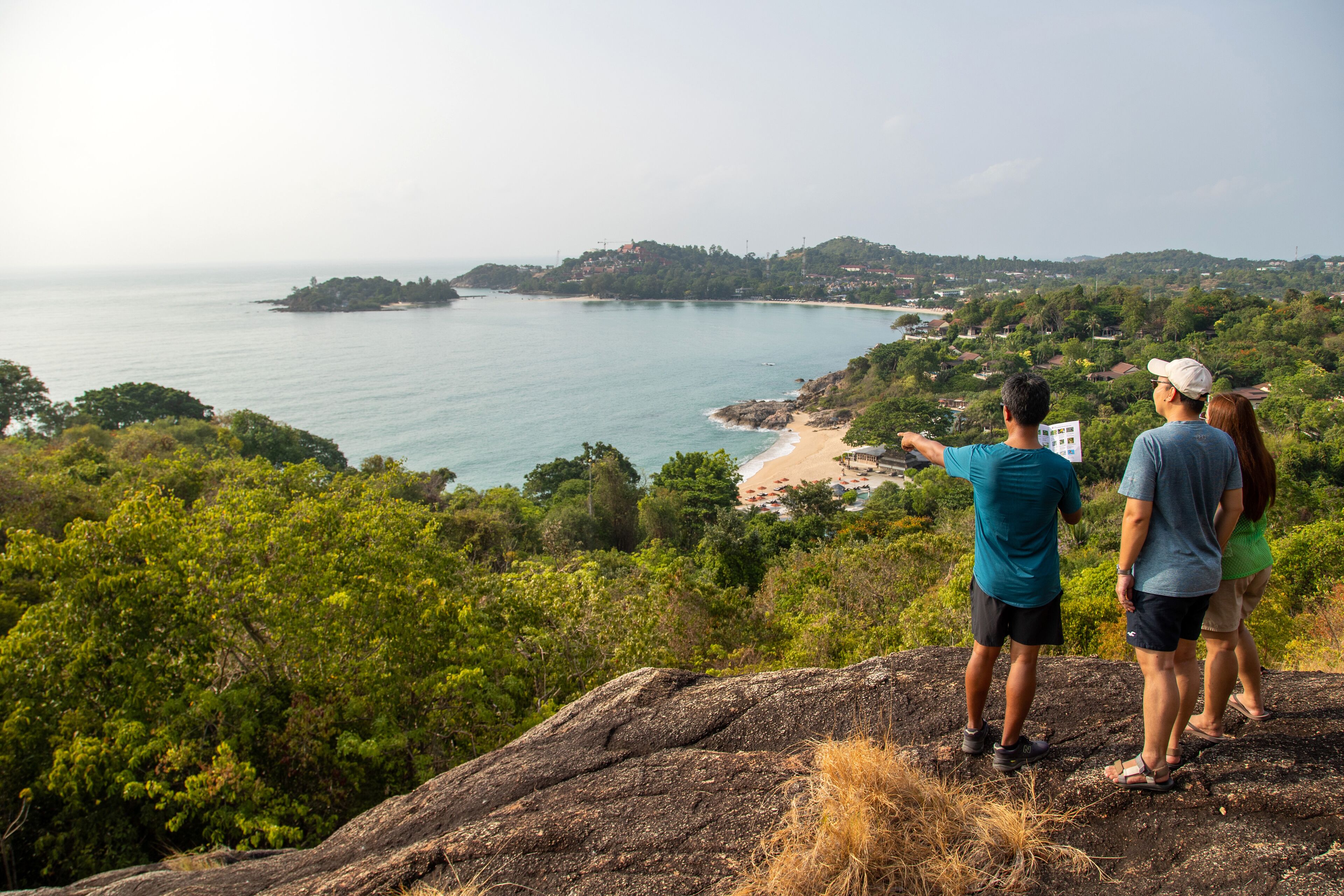 A couple overlooking a coastal landscape with a rocky outcrop in the foreground and a beach in the distance.