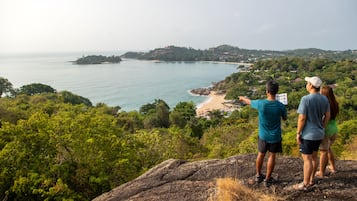 A couple overlooking a coastal landscape with a rocky outcrop in the foreground and a beach in the distance.