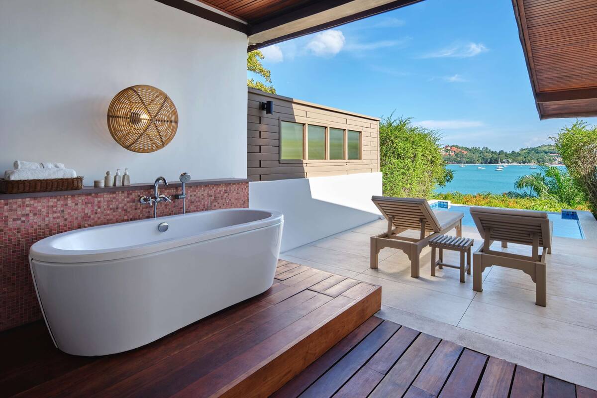 A modern bathroom with a freestanding bathtub, a wicker wall decor, and a view of the sea.