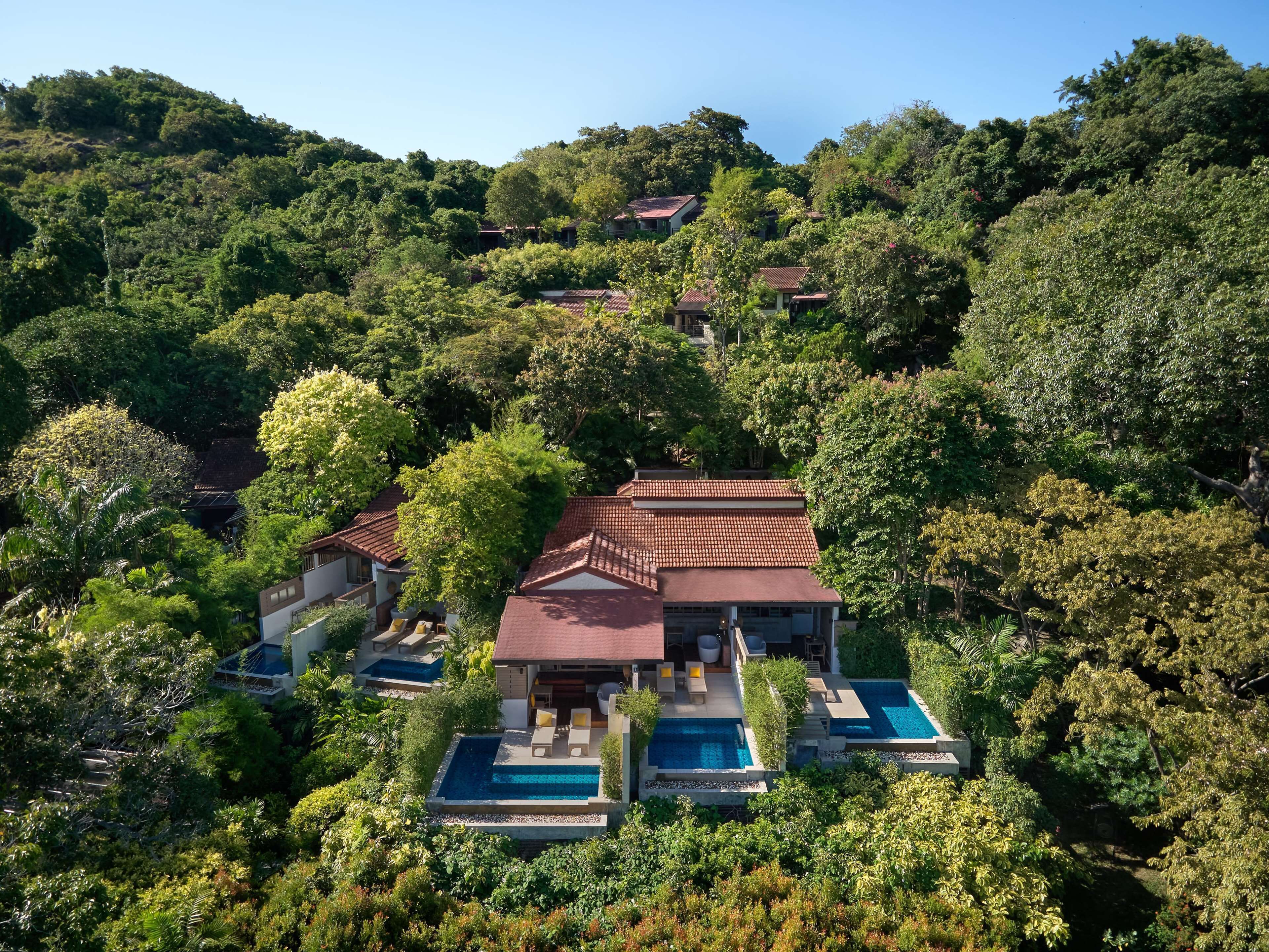 A hillside villa with multiple swimming pools, surrounded by lush greenery and trees.