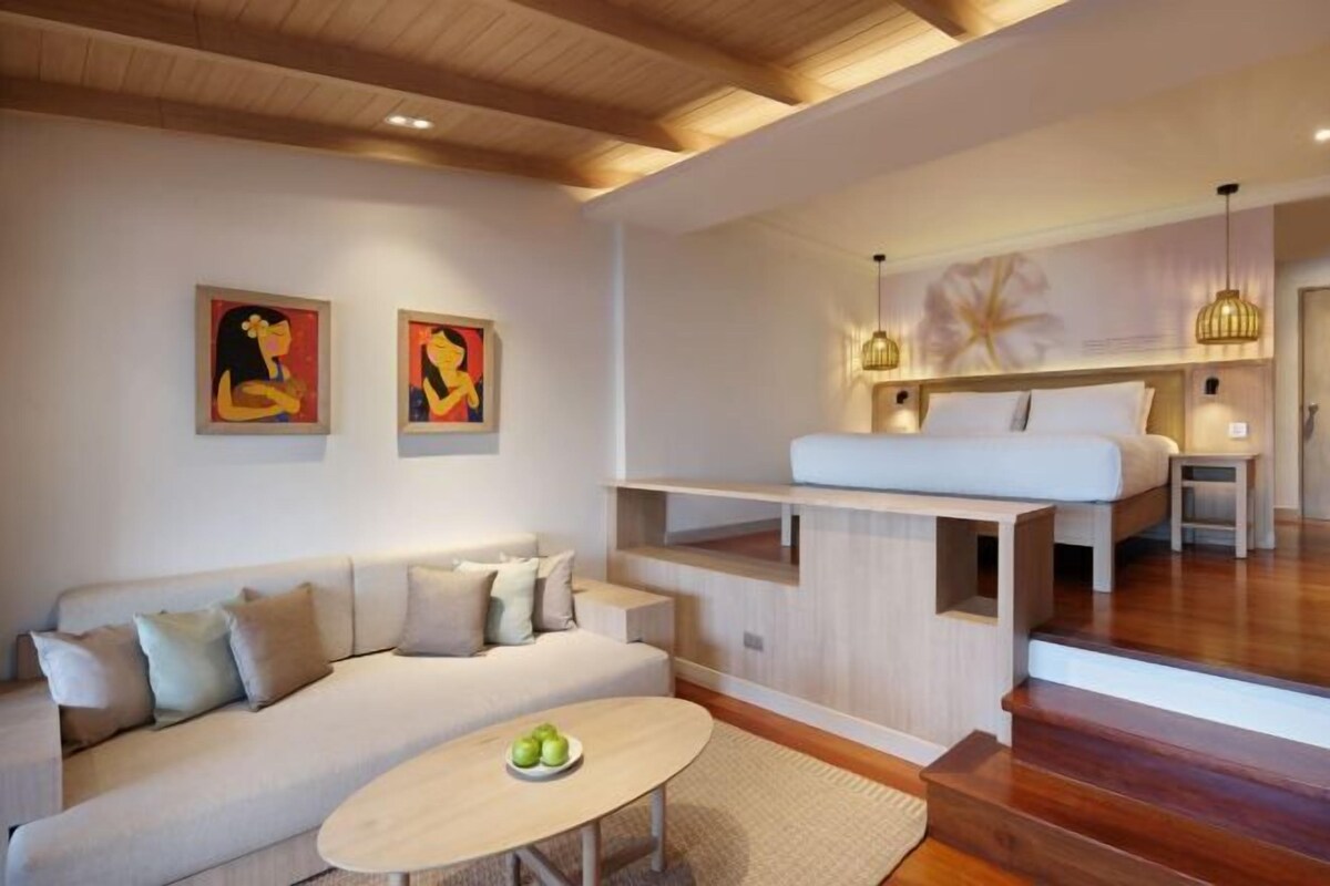 A modern interior with a sofa, a round table, a bed with a headboard, and artwork on the walls.