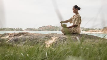 Eine Person sitzt auf einem Felsen am Wasser und hält eine Schüssel.