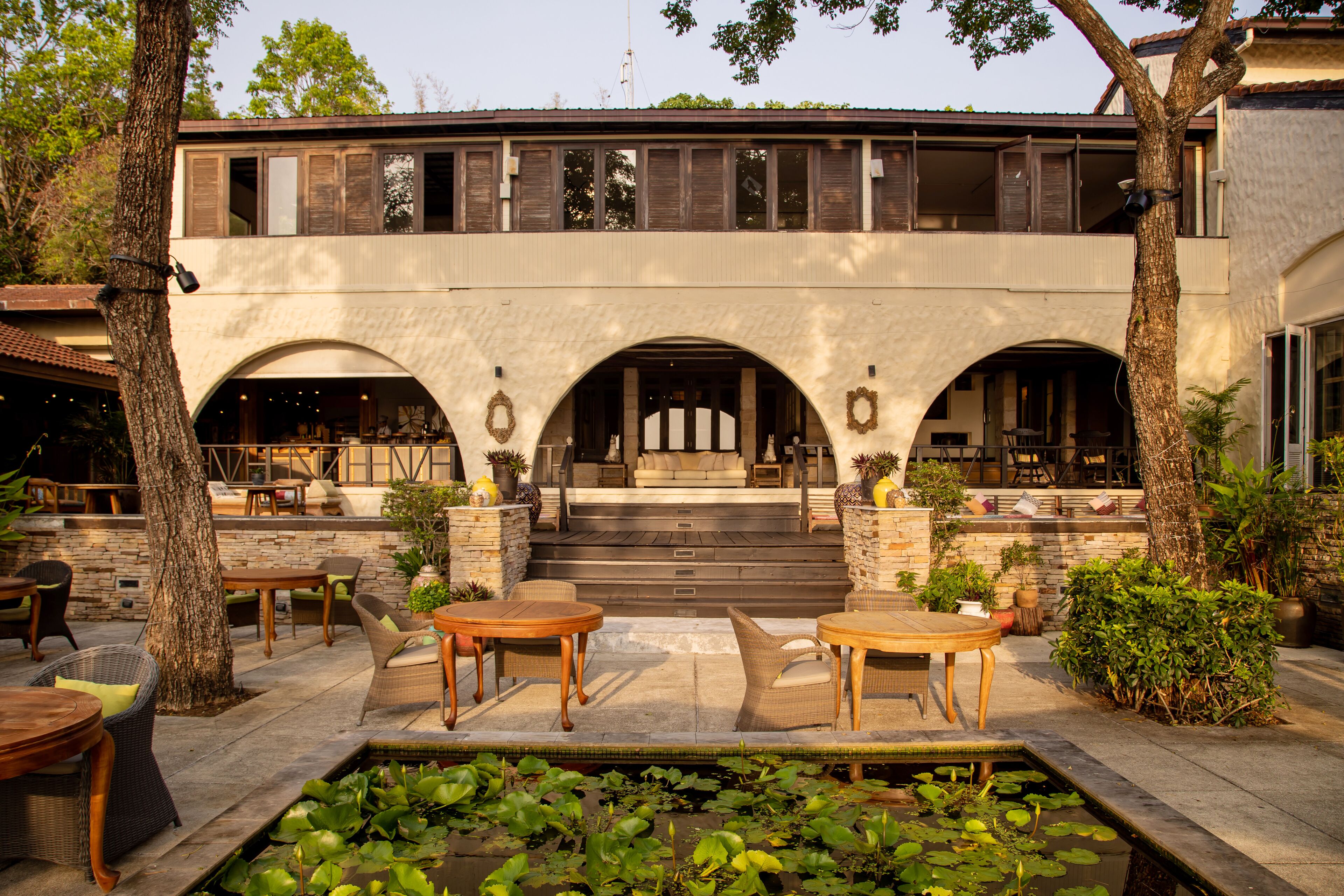 A two-story building with a patio area featuring outdoor seating and a small pond.