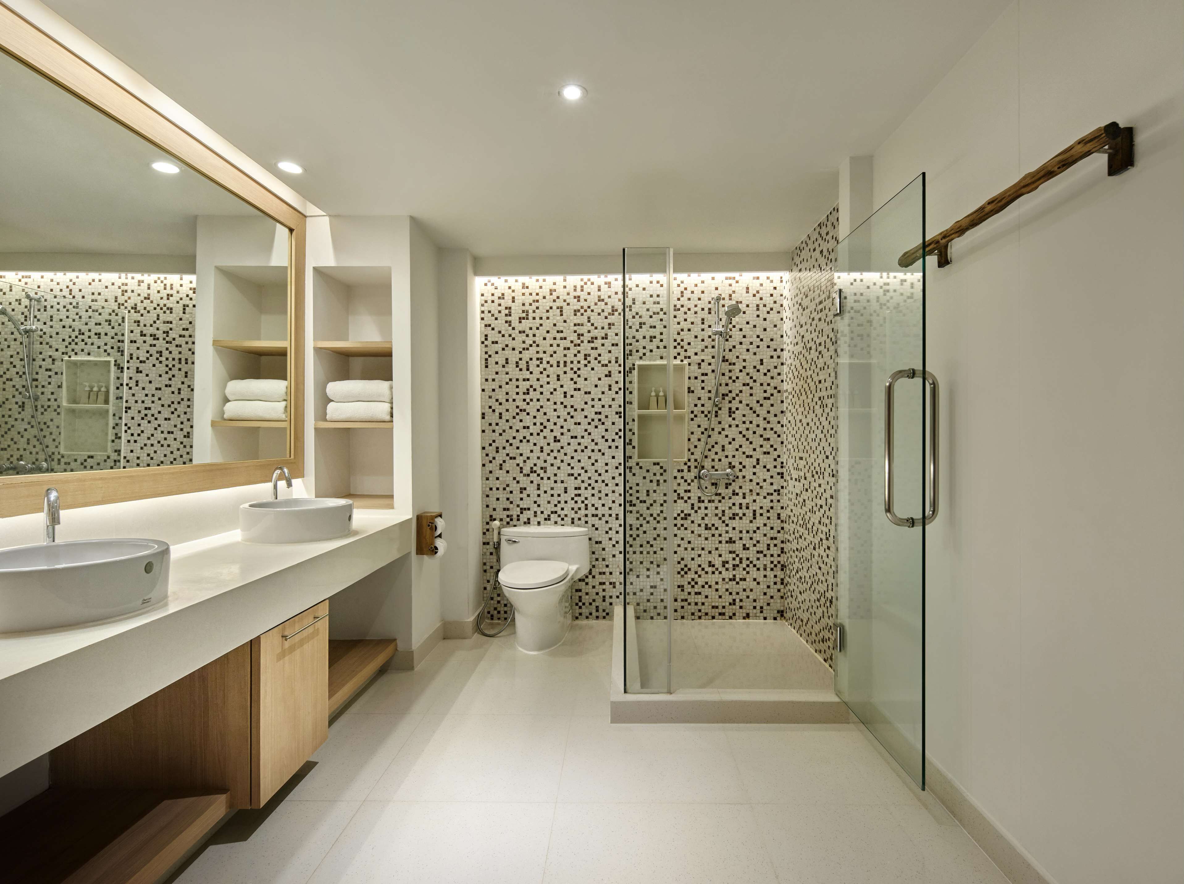 A modern bathroom with a large mirror, two sinks, a toilet, and a glass-enclosed shower.
