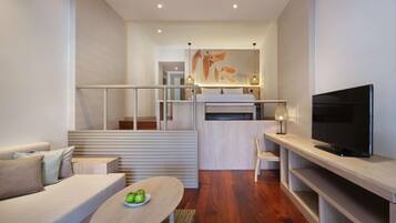 A modern living room with a sofa, a coffee table with apples, a TV, and a staircase leading to an upper level.