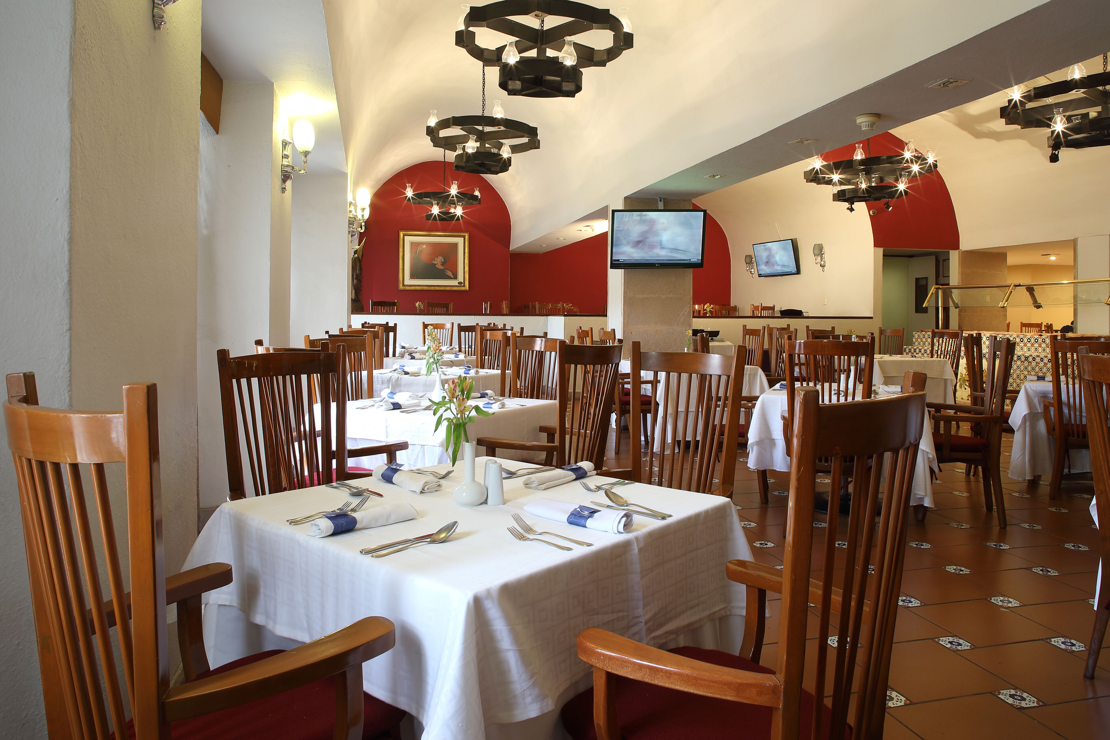 Un restaurante con varias mesas dispuestas para comer, sillas de madera y un televisor montado en la pared.