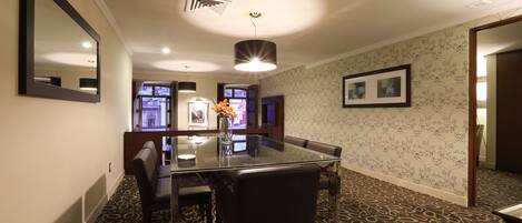 A dining area with a glass table, leather chairs, patterned carpet, and a wall-mounted mirror.