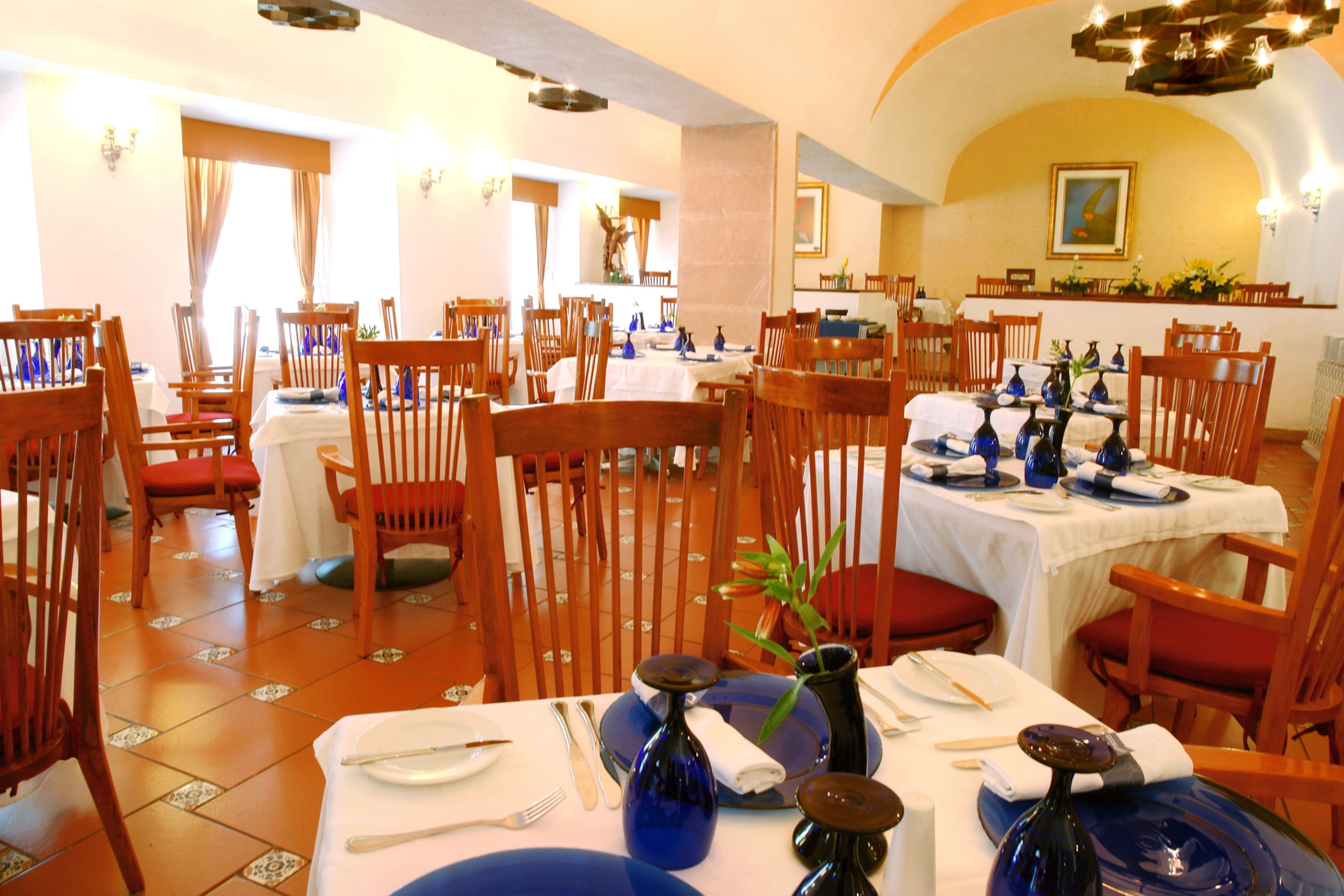 Un restaurante con varias mesas dispuestas para comer, sillas de madera y piso de baldosas.