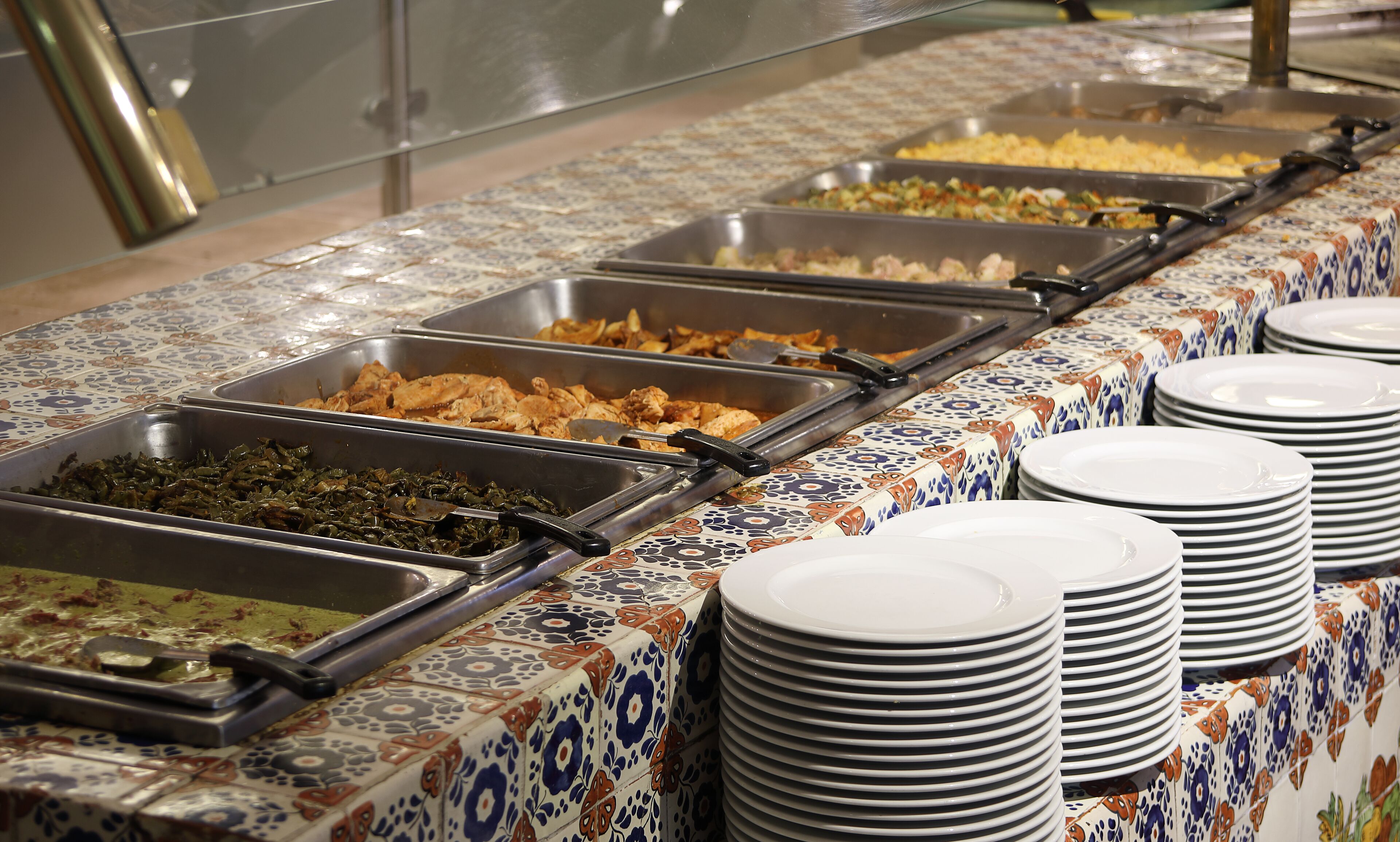 A buffet with various food options and stacked white plates.