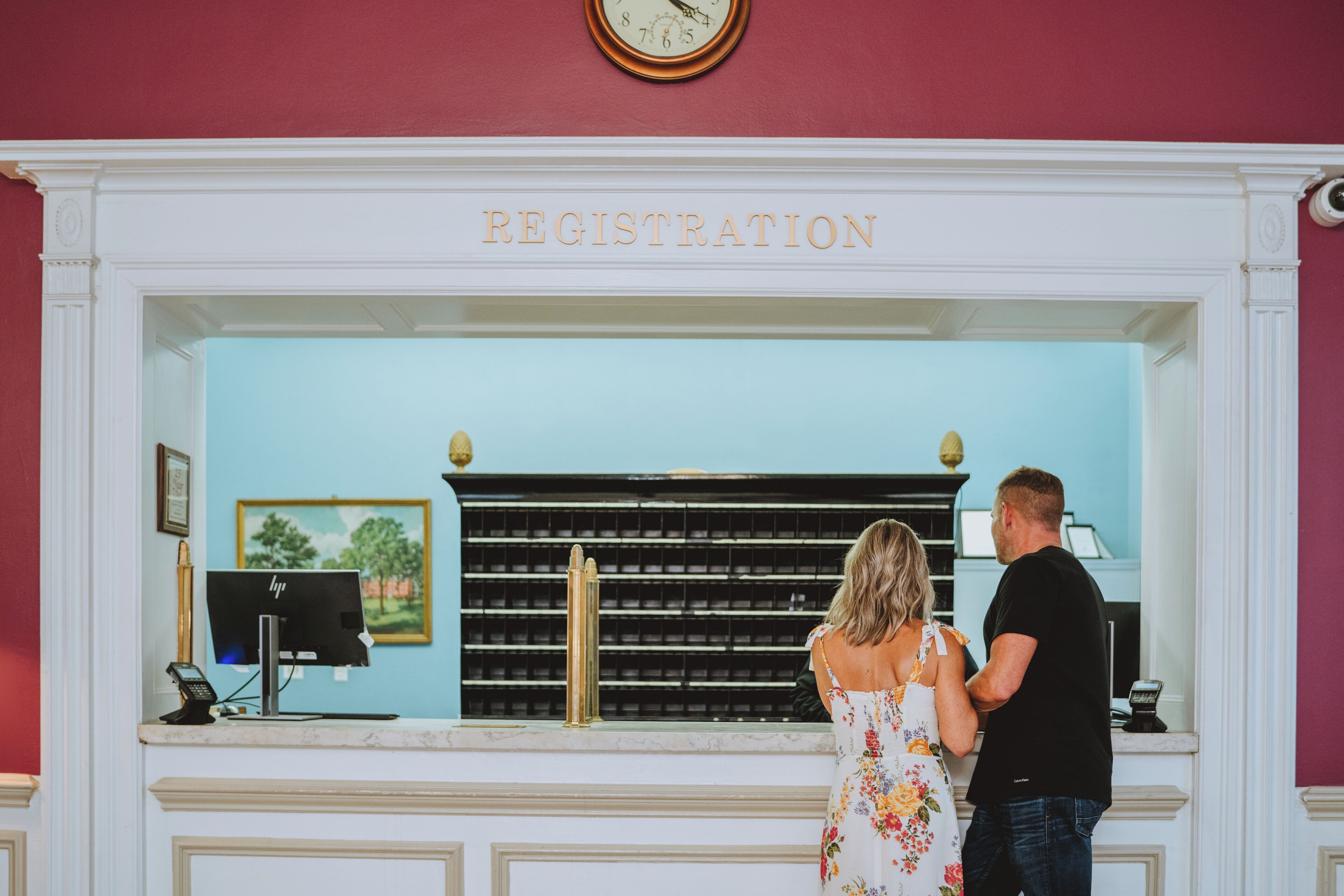 A registration desk with a computer and a phone, a clock above it, and a wall with a framed picture.