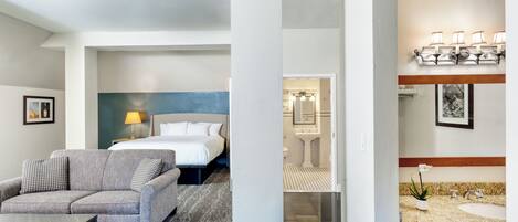 A hotel room with a bed, a sofa, a coffee table, and a bathroom with a sink and mirror.