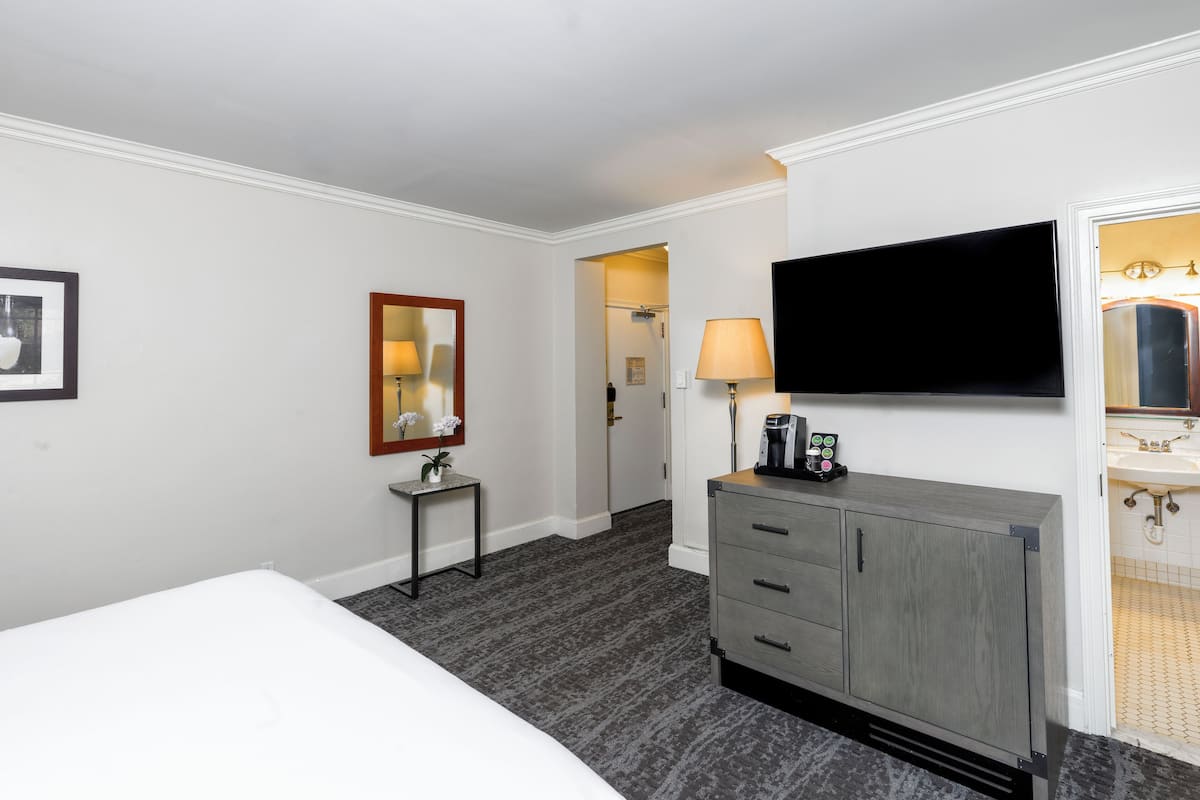 Une chambre d’hôtel avec un lit, une petite table avec une lampe, un téléviseur fixé au mur et une commode avec des tiroirs.