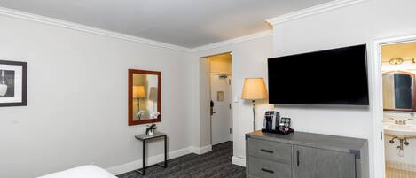 Una habitación de hotel con cama, una mesita de noche con lámpara, un televisor montado en la pared y un armario con cajones.