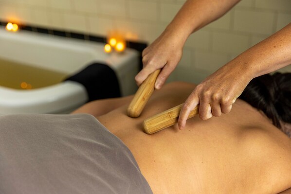 A person receiving a back massage in a room with a bathtub and candles.