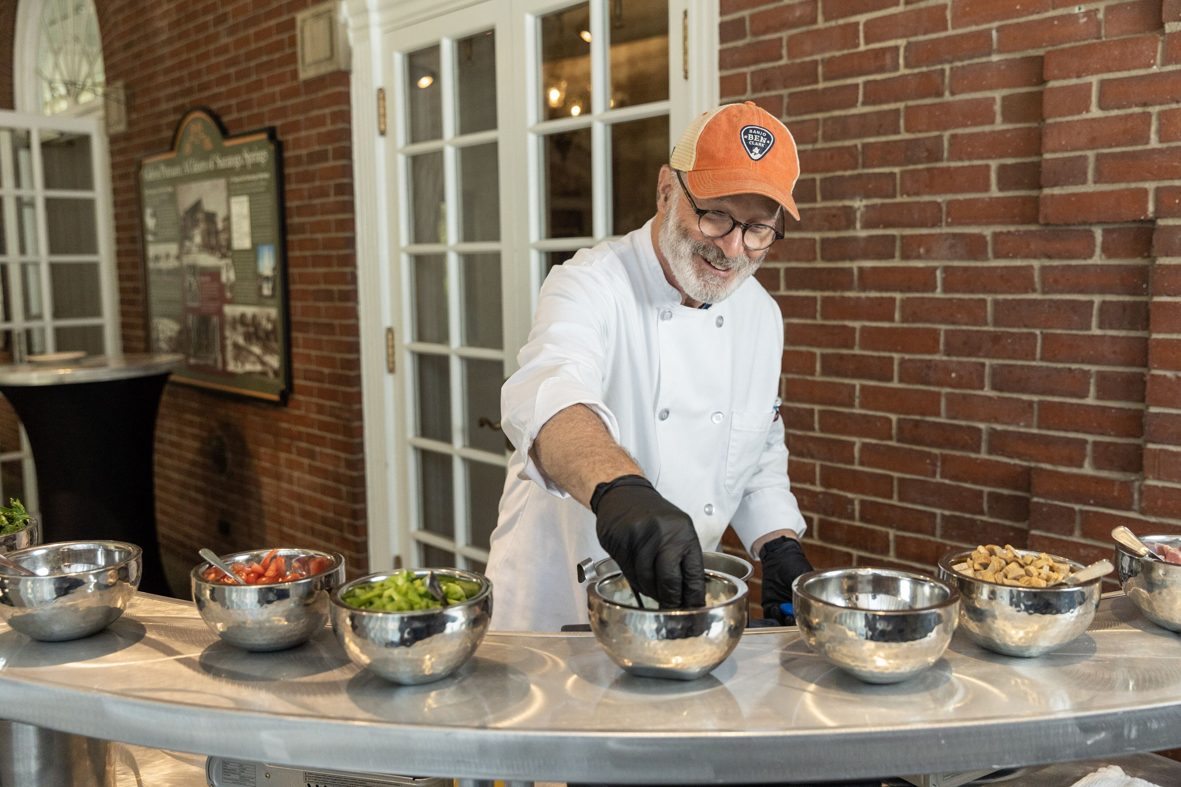 A chef preparing food in a kitchen with a brick wall and a door in the background.