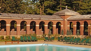 Un espace piscine avec un bâtiment en briques doté d’arches et d’un toit recouvert de tuiles.