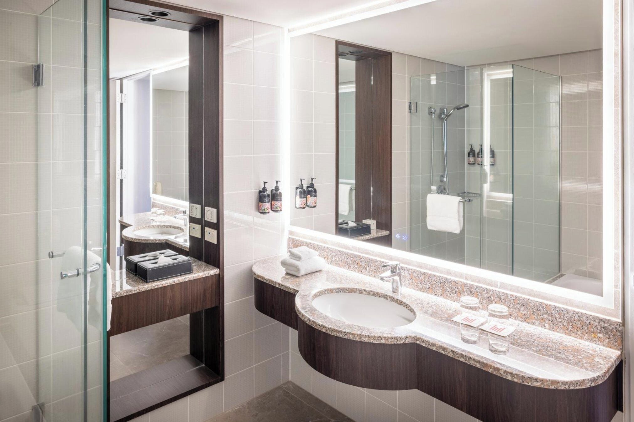 A modern bathroom with two sinks, a large mirror, and a glass shower enclosure.