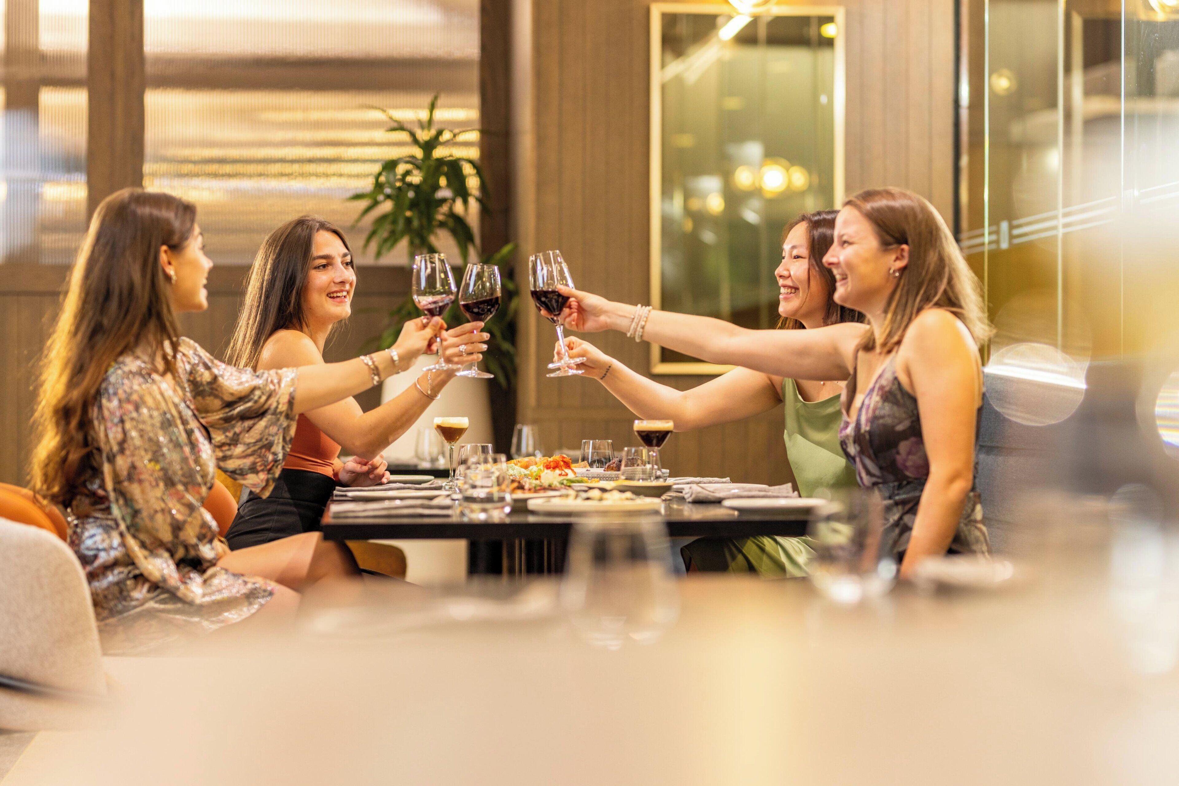 A group of people toasting with wine glasses at a dining table in a well-lit indoor setting.