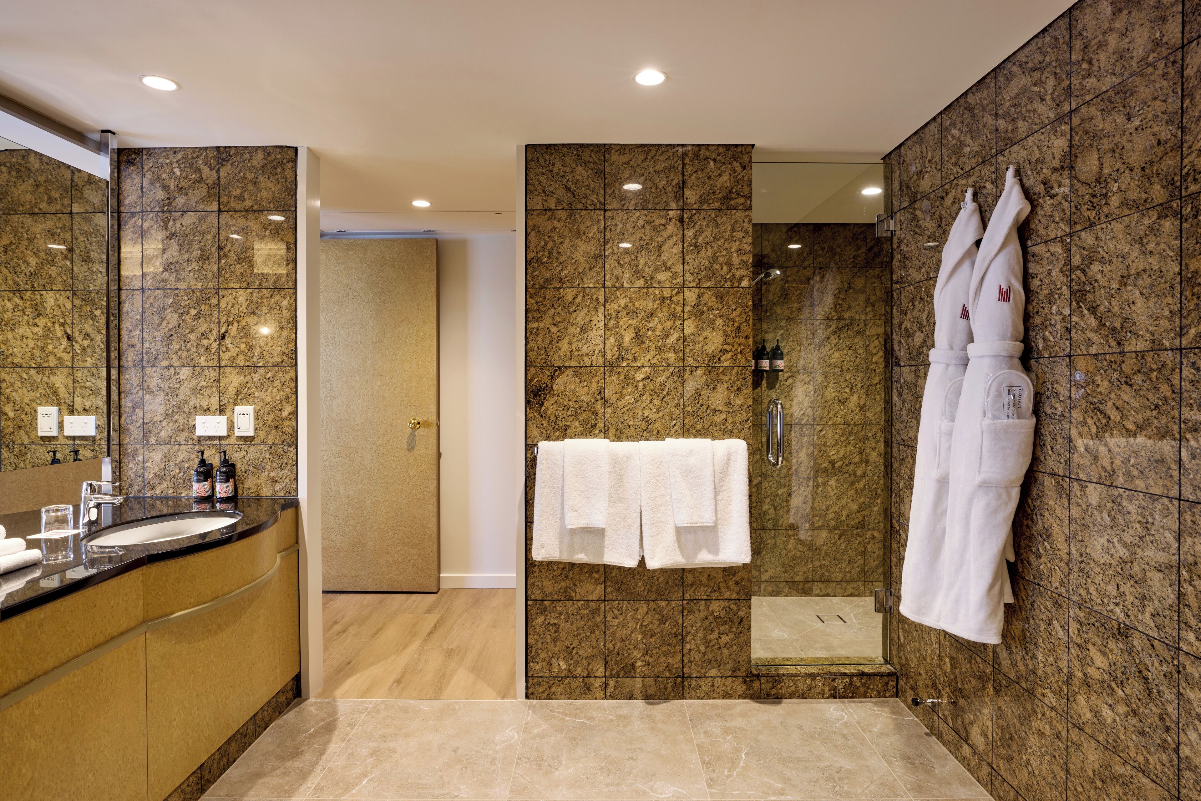A modern bathroom with a marble wall, a sink with toiletries, and a glass shower enclosure.