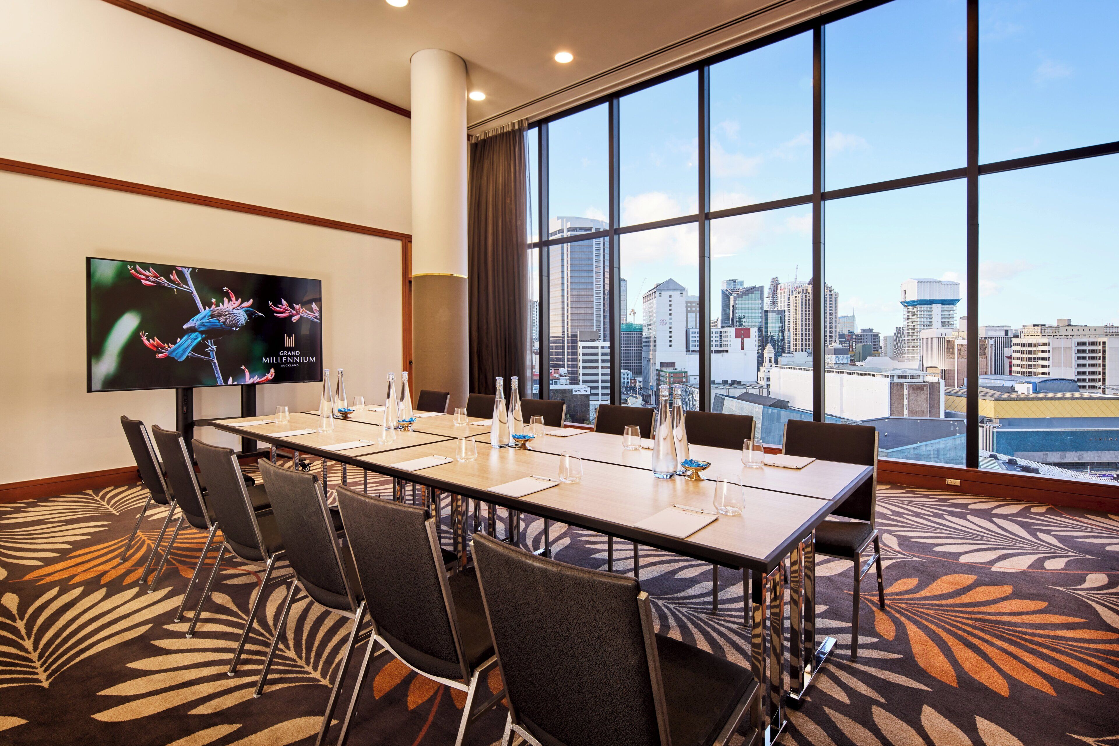 A conference room with a city view, large windows, and a flat-screen TV on the wall.