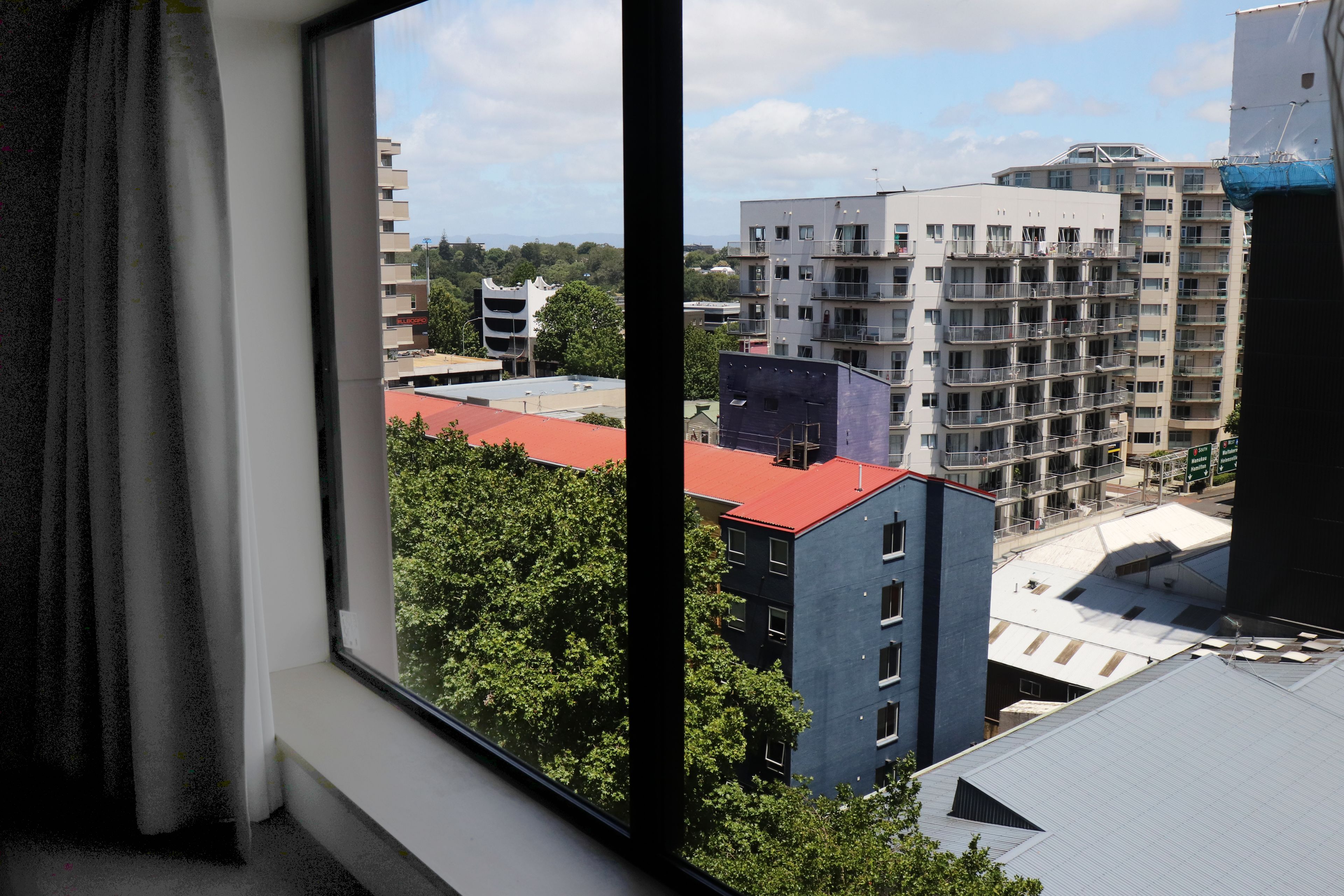 Vista dalla finestra su una città con numerosi edifici, tra cui una struttura bianca particolare e un palazzo con tetto rosso.