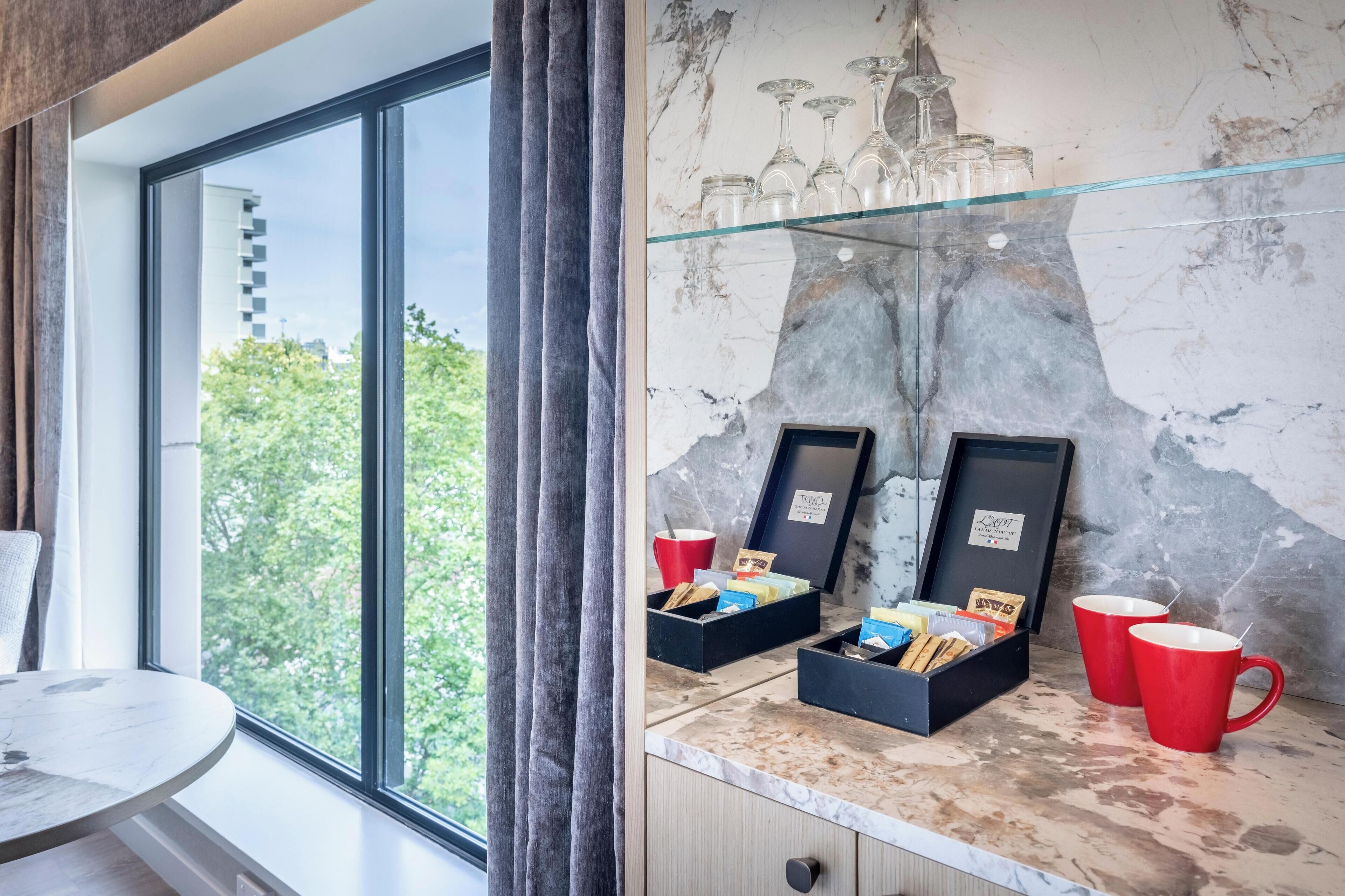Quarto moderno com uma janela grande, bancada de mármore e prateleira de vidro com copos de vinho e xícaras.