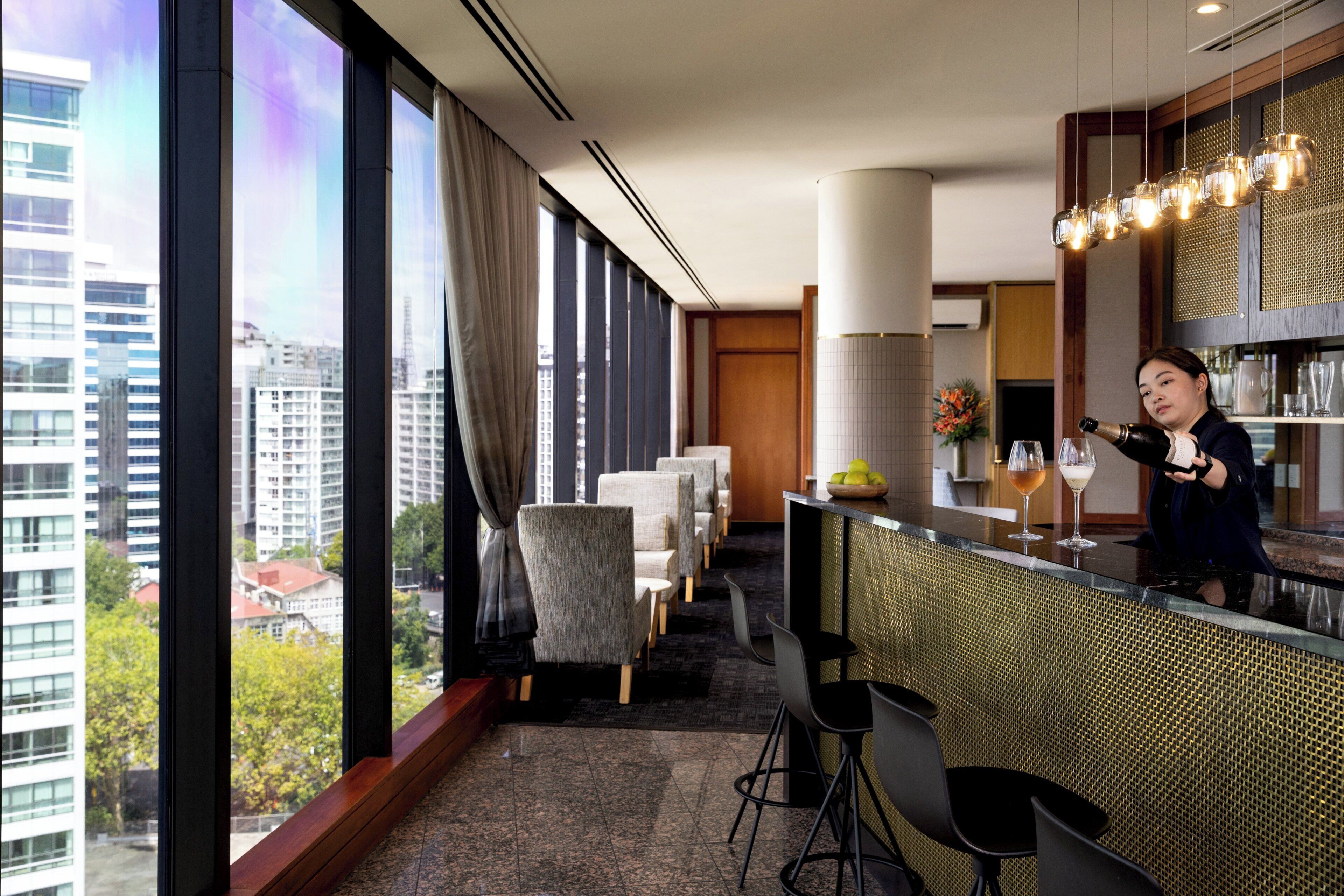A modern hotel bar with large windows, a bar counter, and seating area.