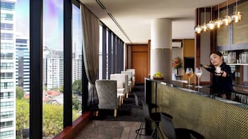 A modern hotel bar with large windows, a bar counter, and seating area.