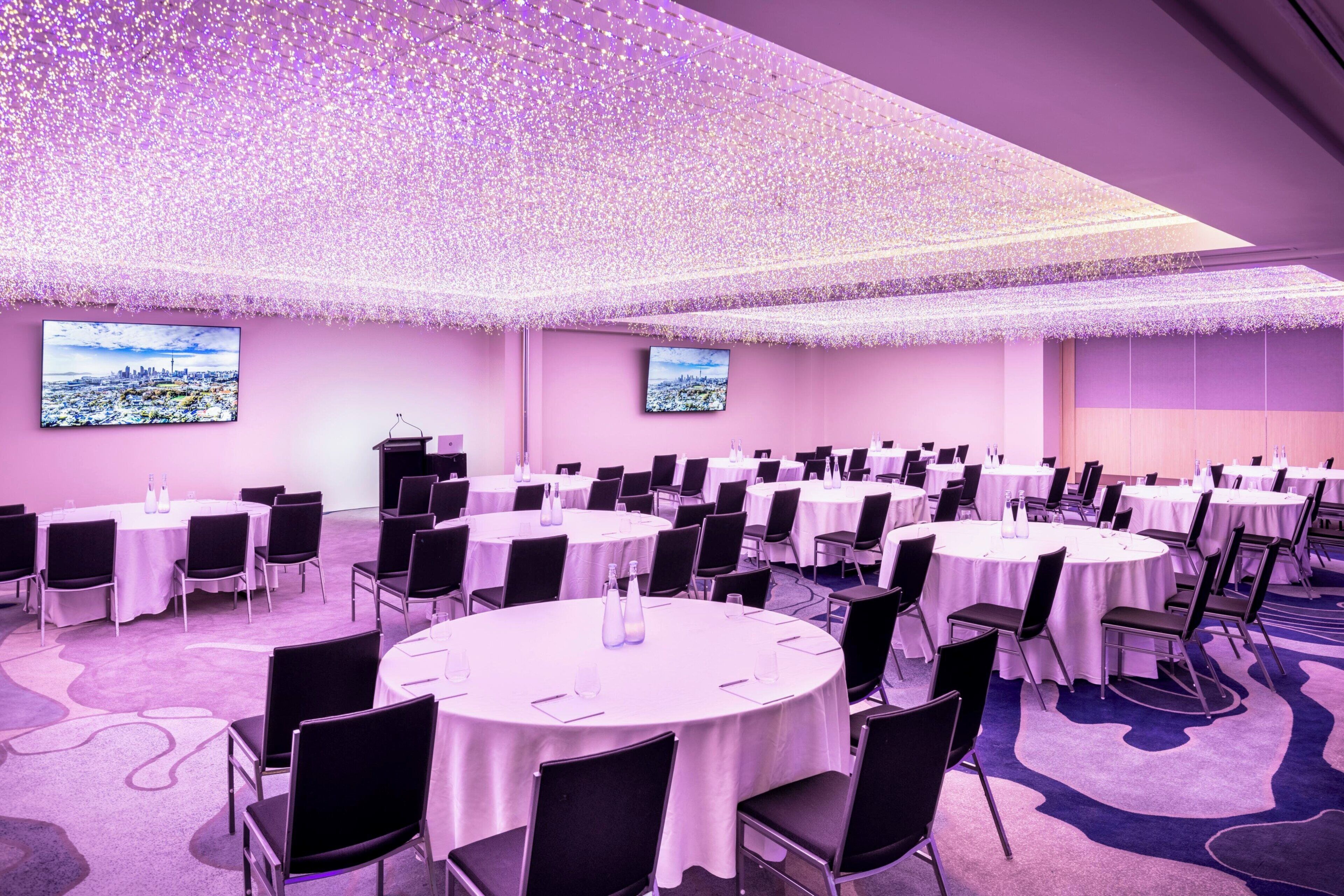 Un salón de conferencias con varias mesas redondas, sillas negras y un techo decorado con luces.