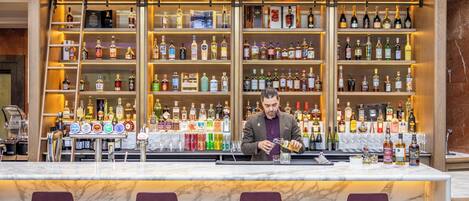 Eine Bar mit einem Barkeeper, der ein Getränk zubereitet, Regalen voller Spirituosenflaschen und Marmor-Barhocker.