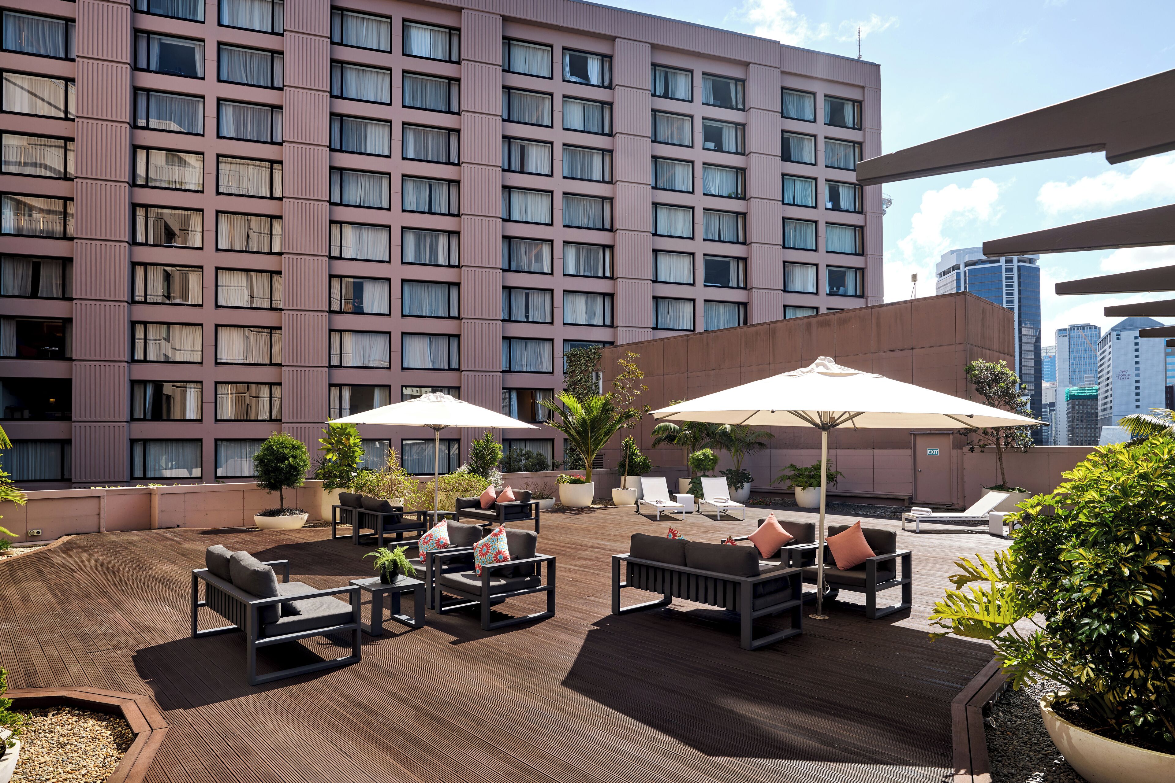 A rooftop terrace with outdoor seating, potted plants, and a view of a high-rise building.