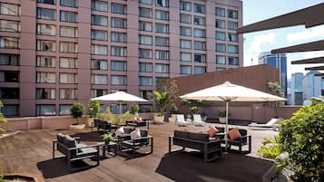 A rooftop terrace with outdoor seating, potted plants, and a view of a high-rise building.