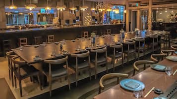 A restaurant with long communal tables, chairs, and hanging lights.