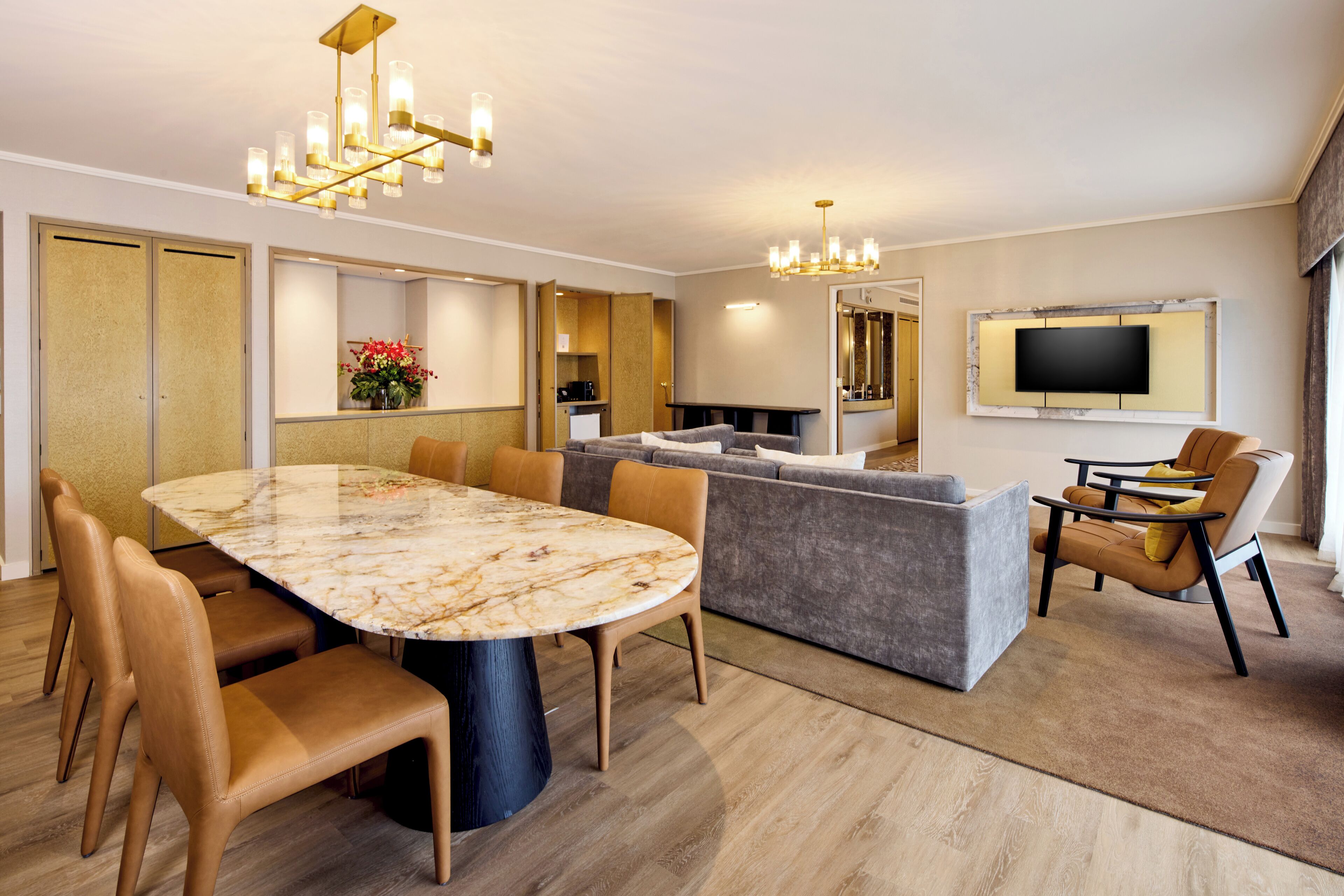A modern living room with a marble dining table, leather sofas, and a TV mounted on the wall.