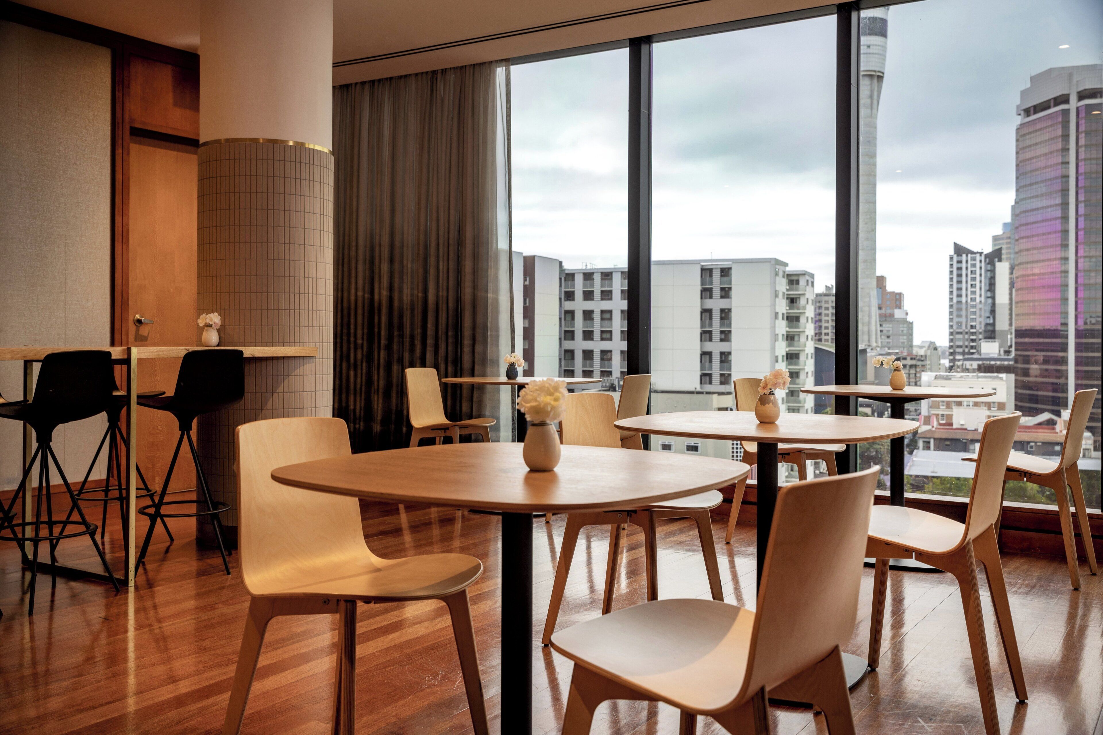 Ein modernes Hotelzimmer mit großen Fenstern und Blick auf die Stadt, Holzboden und einer Mischung aus modernen und klassischen Möbeln.