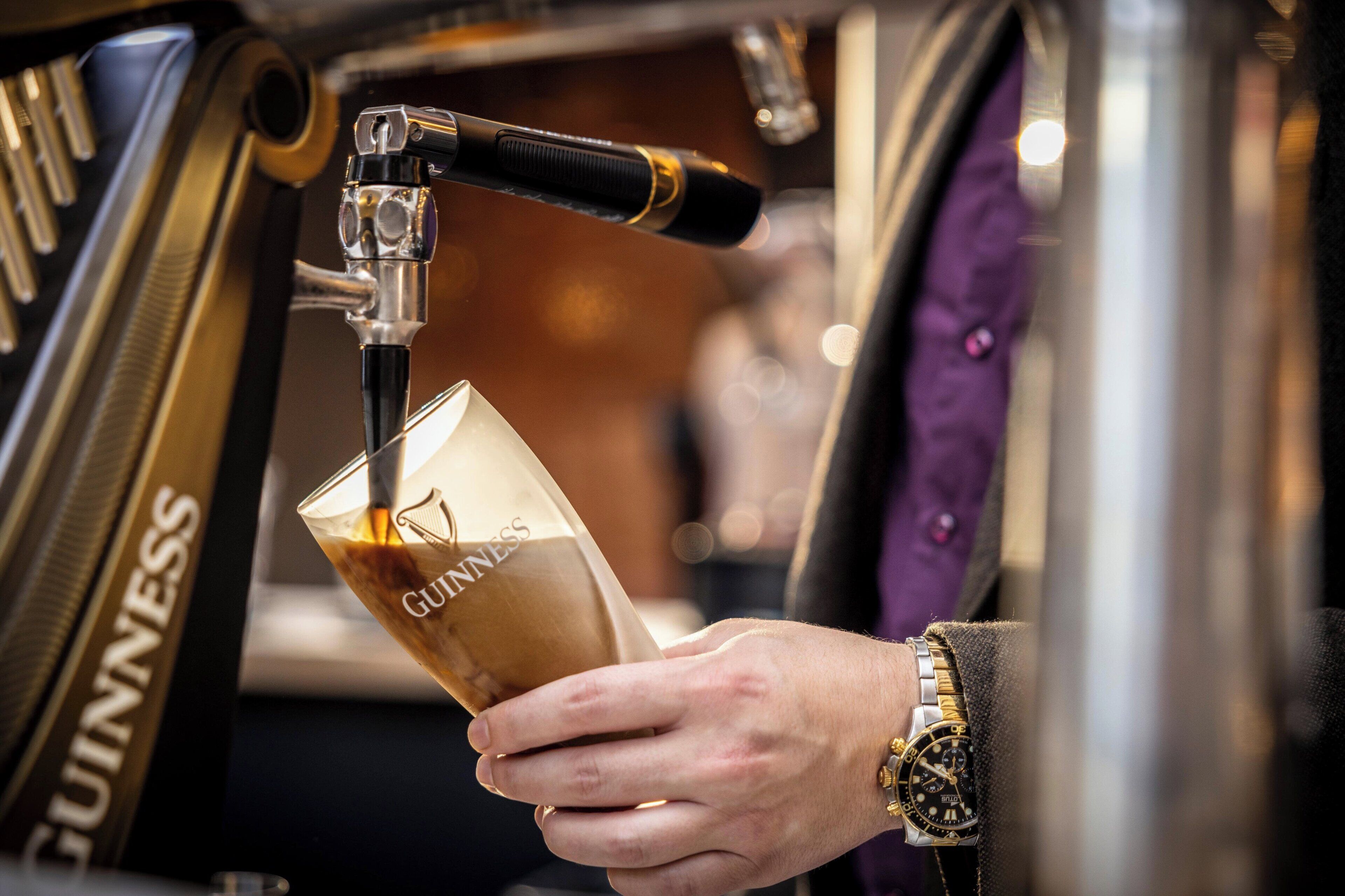 A person pouring Guinness beer from a tap into a glass.