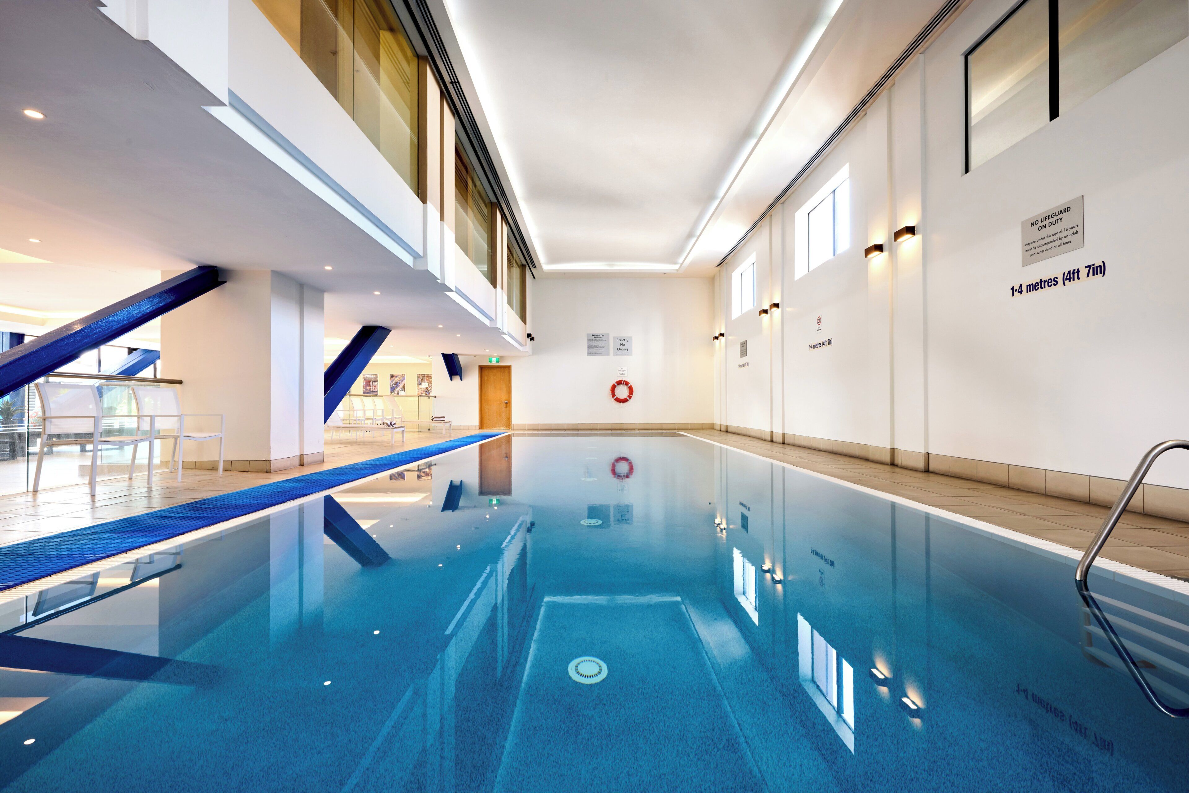 A modern indoor swimming pool with clear signage indicating no lifeguard on duty and a depth of 1-4 meters.