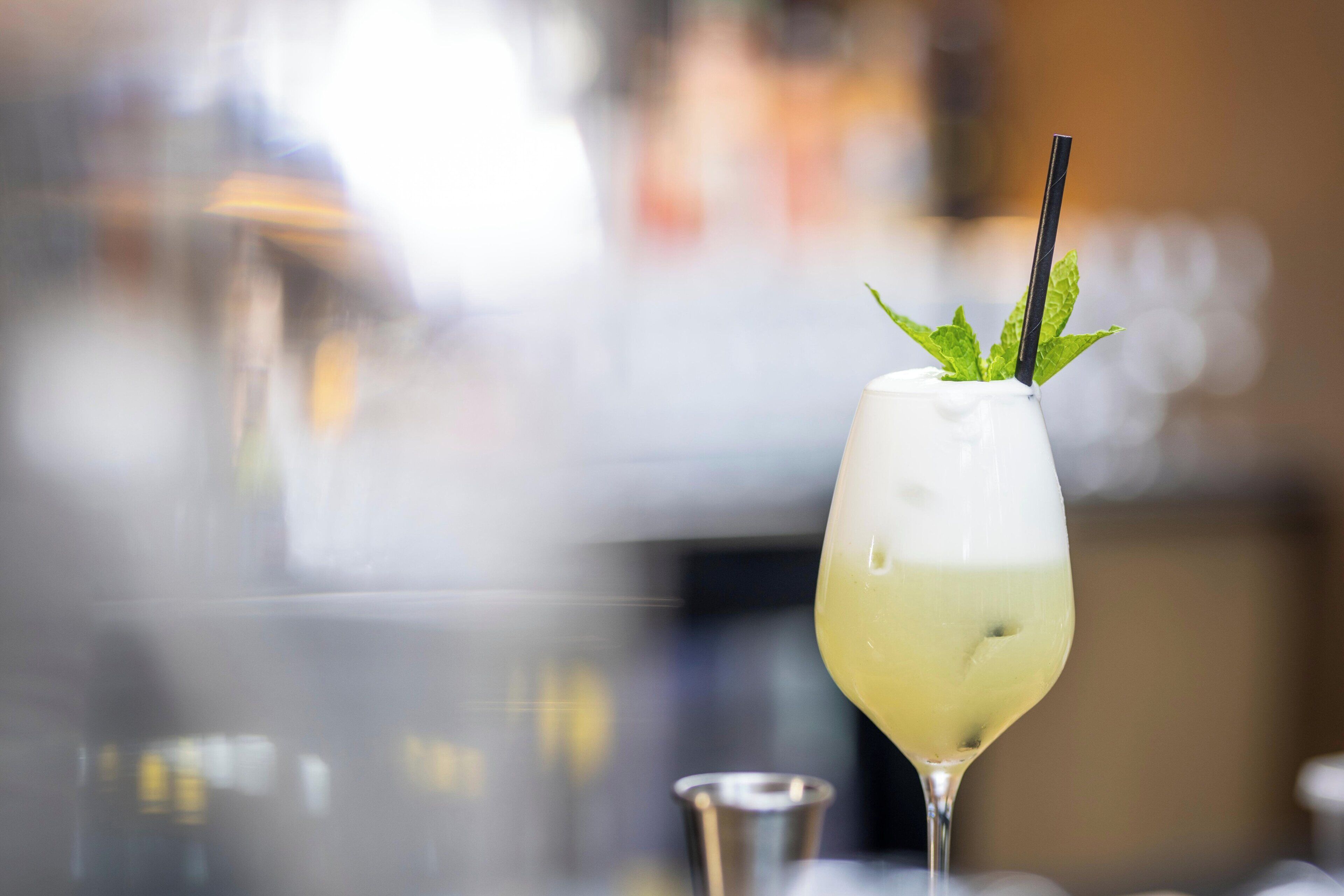 A cocktail glass with a straw and mint leaves on a bar counter.