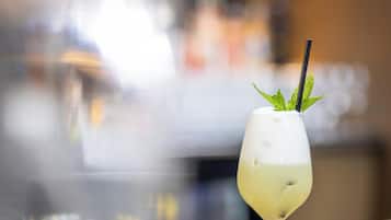 Un verre à cocktail avec une paille et des feuilles de menthe, posé sur le comptoir d’un bar.