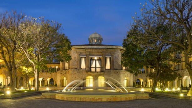A historic building with a central dome, arched windows, and a fountain in the courtyard.